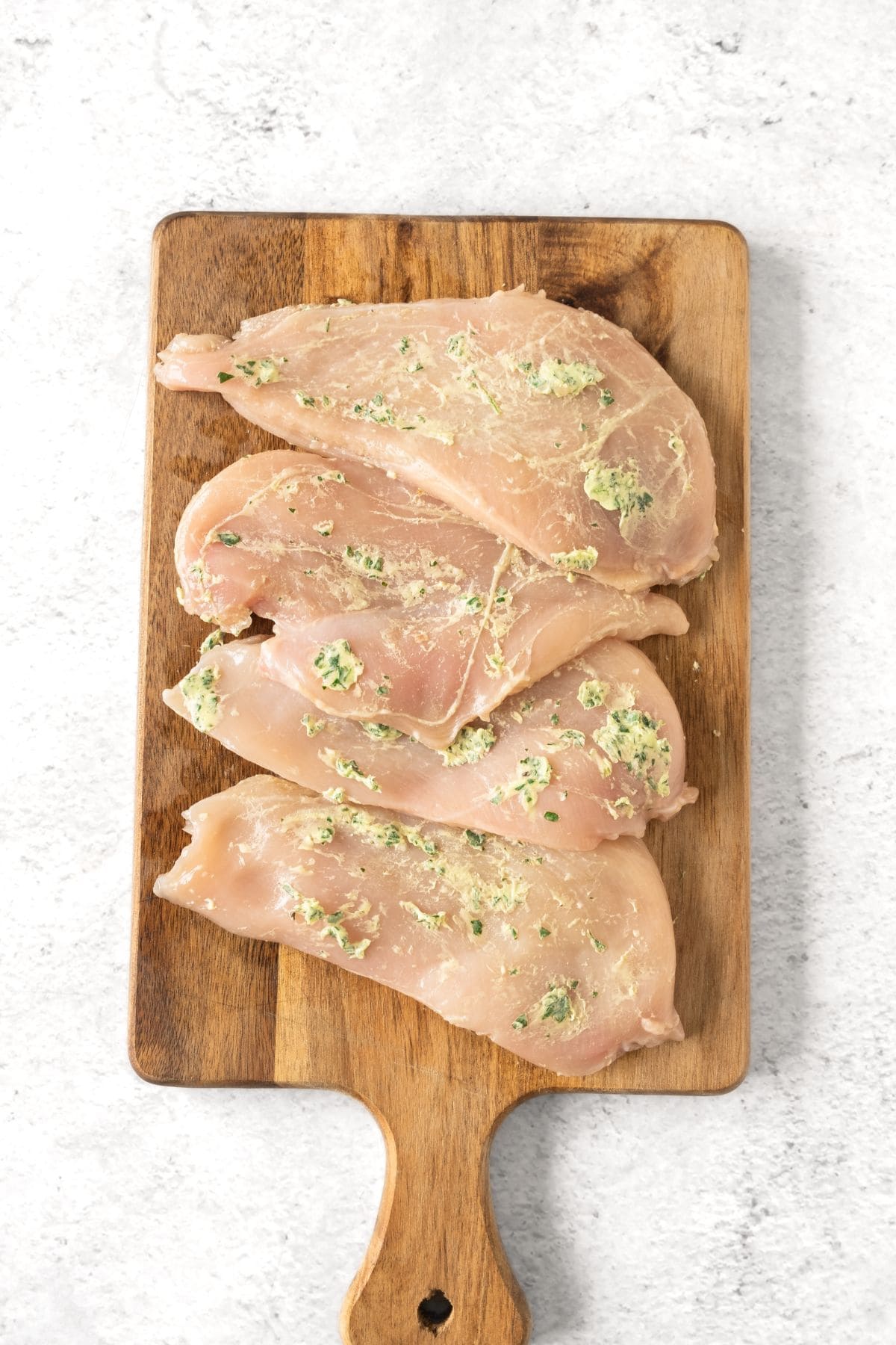 Chicken breasts spread with parsley garlic butter on wooden board.