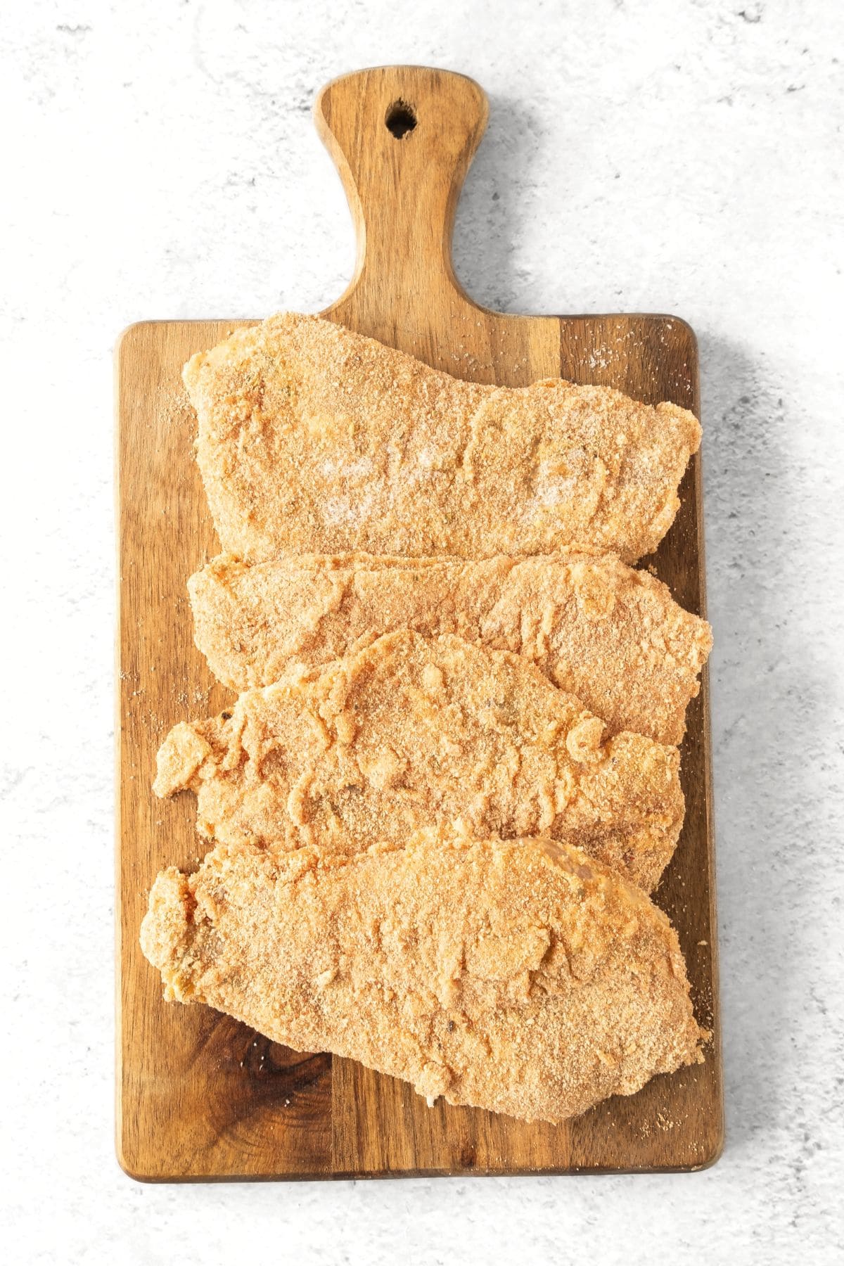 Uncooked breaded chicken cutlets on wooden board.