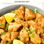 A bowl of lemon chicken topped with green onions.