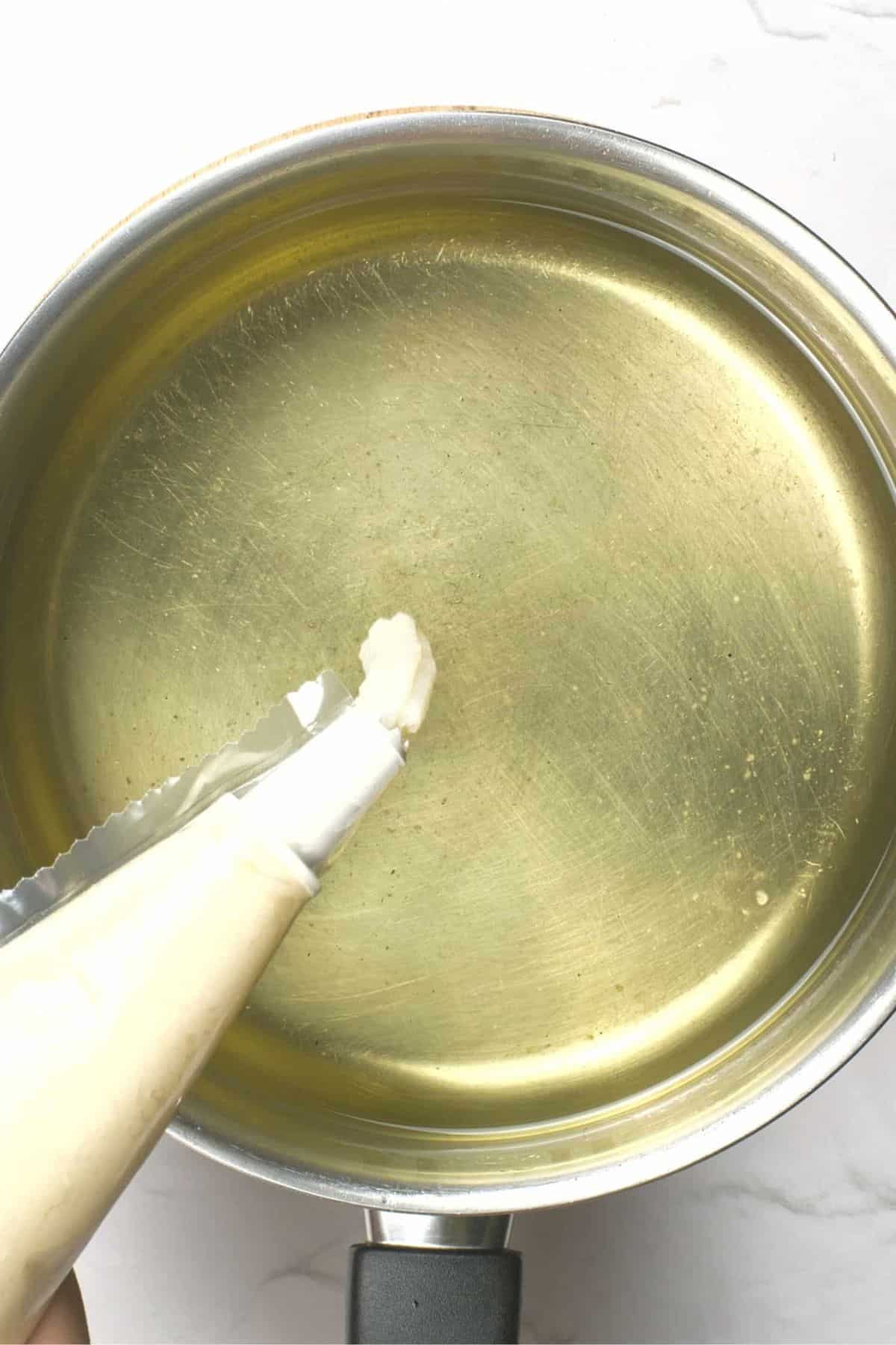 Piping churro dough into a pot of hot oil.