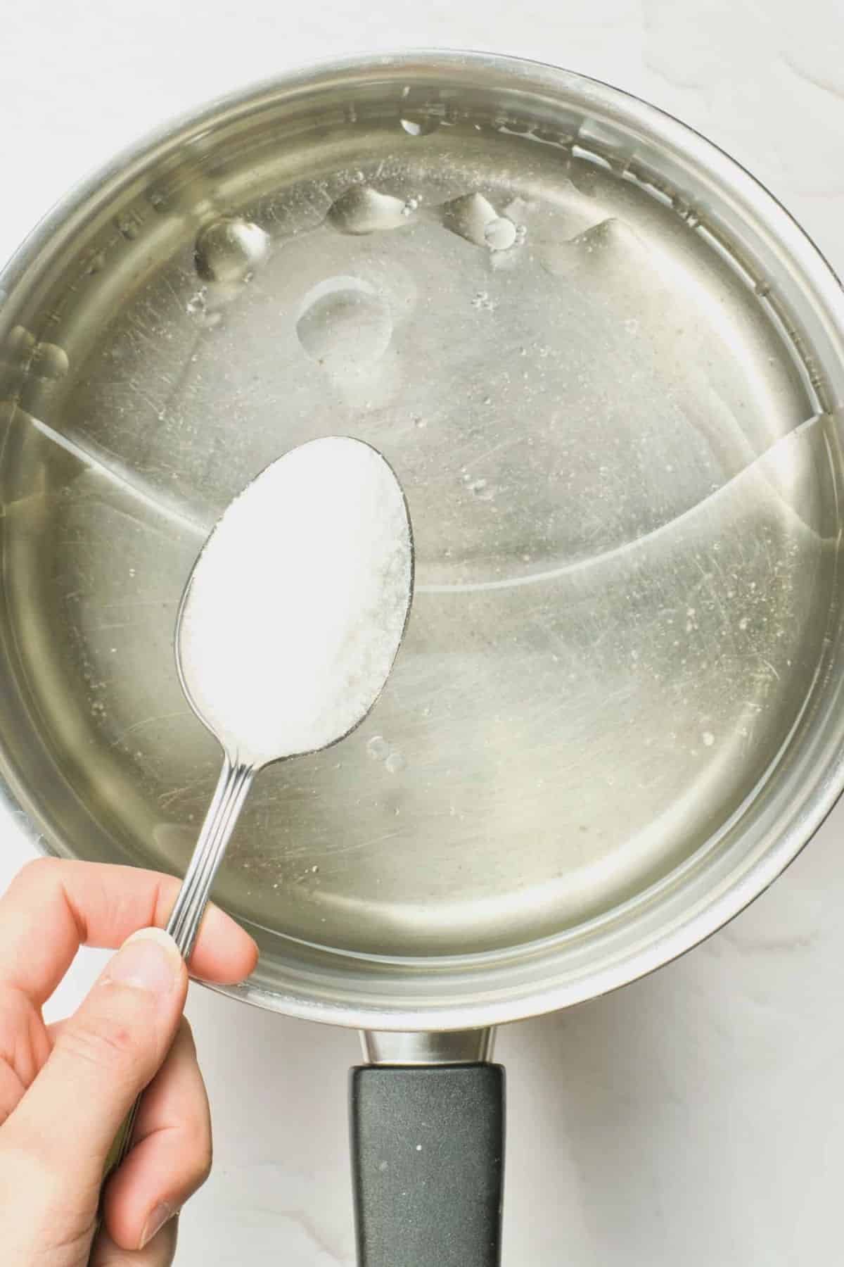 Pouring a spoonful of sugar into a pot of water.