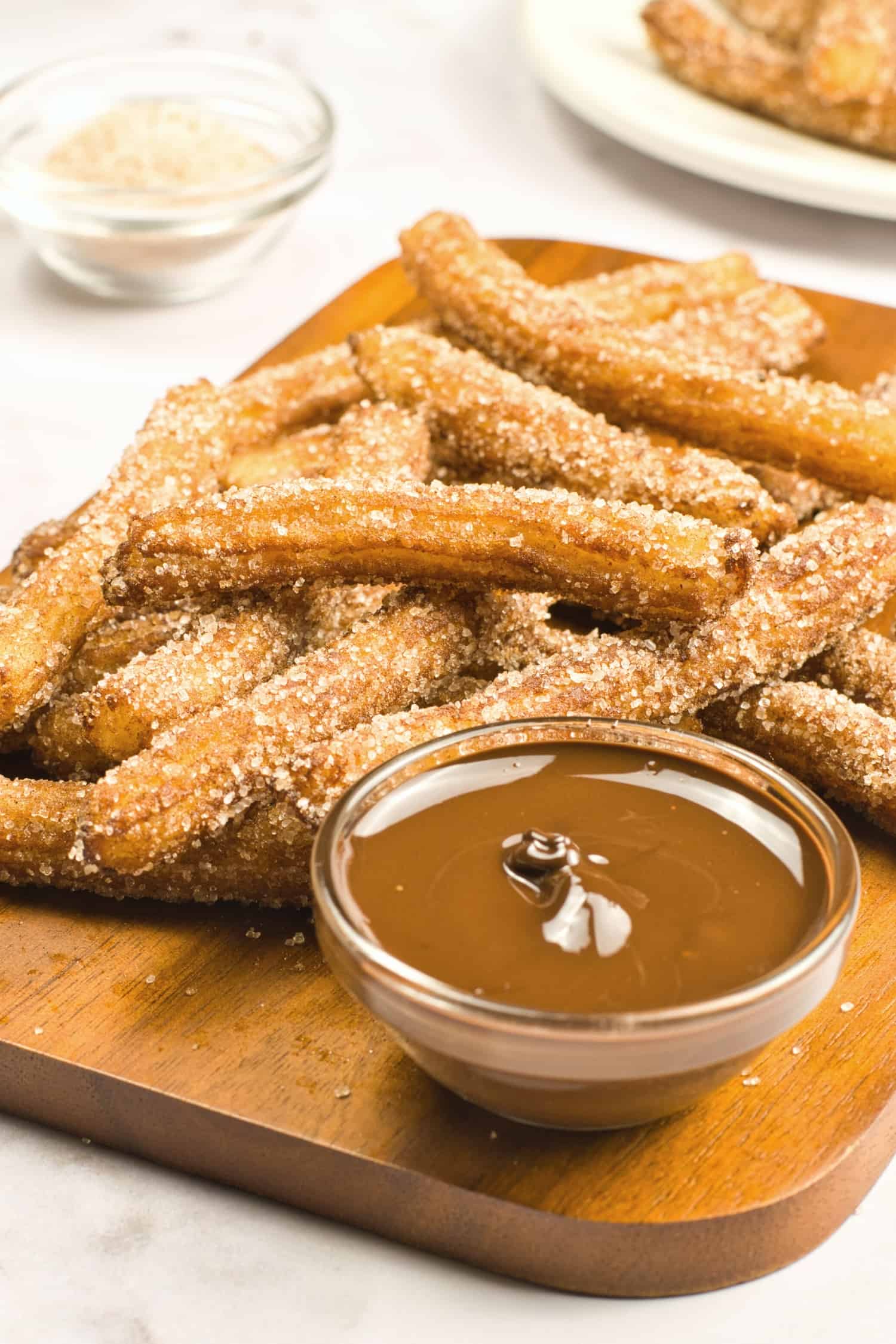 Gluten-free churros and a small bowl of melted chocolate on wooden board.