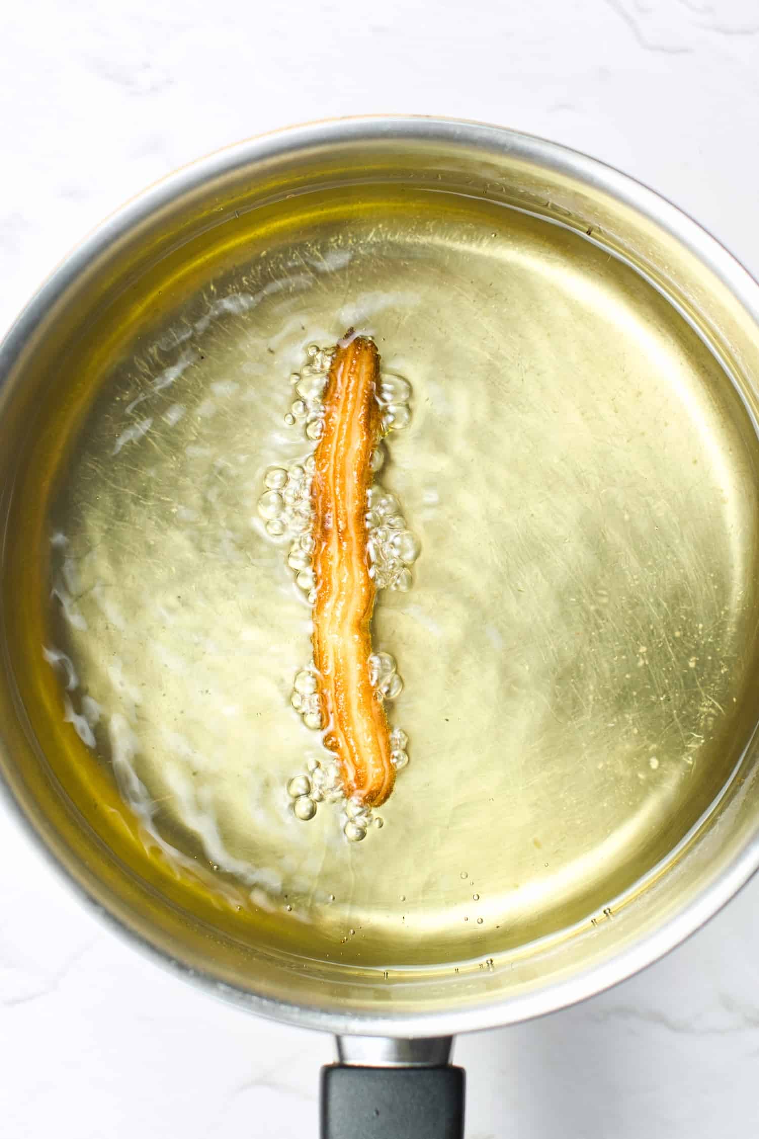 Golden brown churro cooking in hot oil.