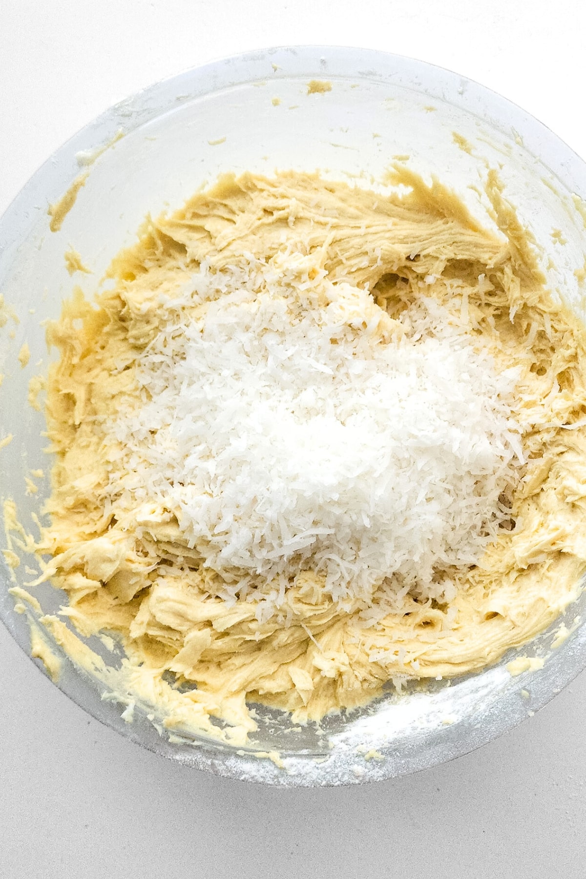 Shredded coconut on top of cake batter in glass bowl.