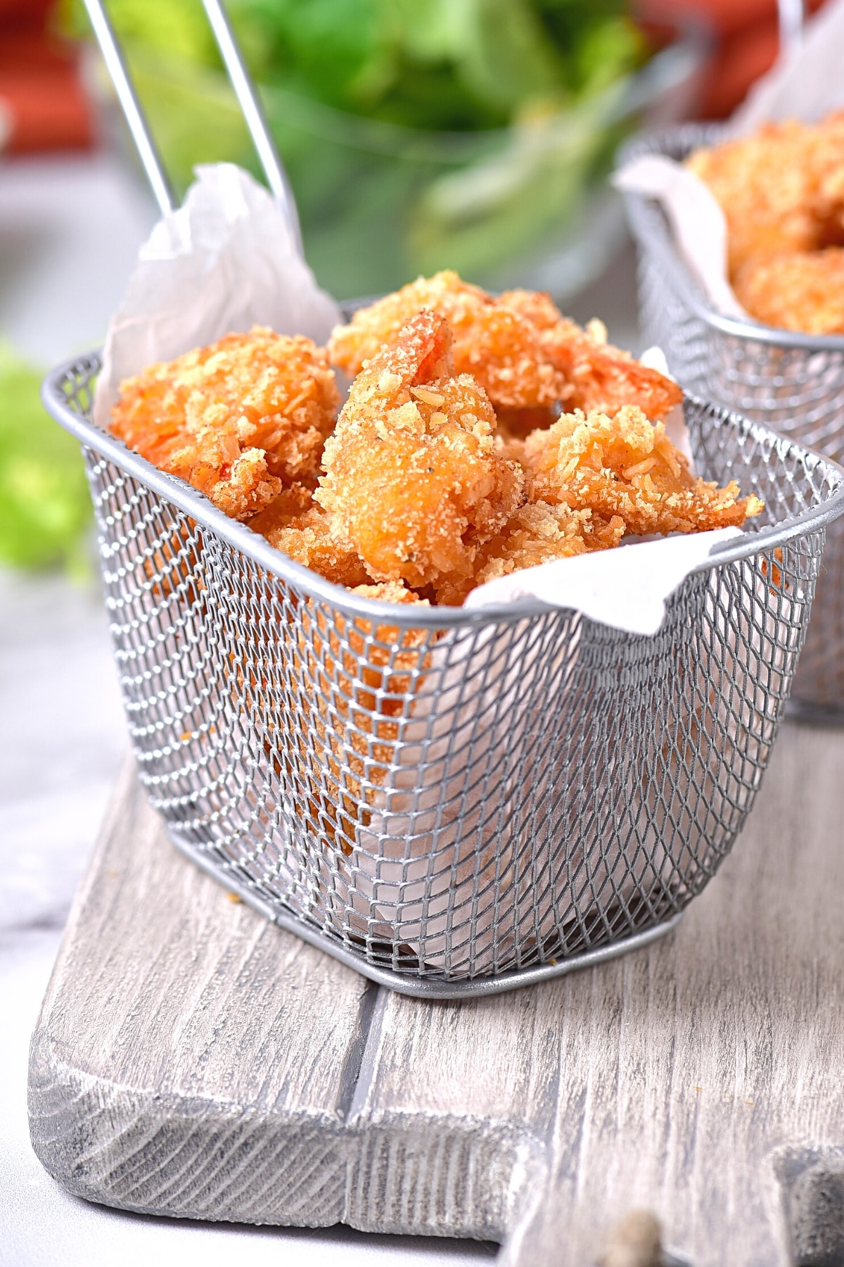 A basket of crispy gluten-free fried shrimp on wooden board.