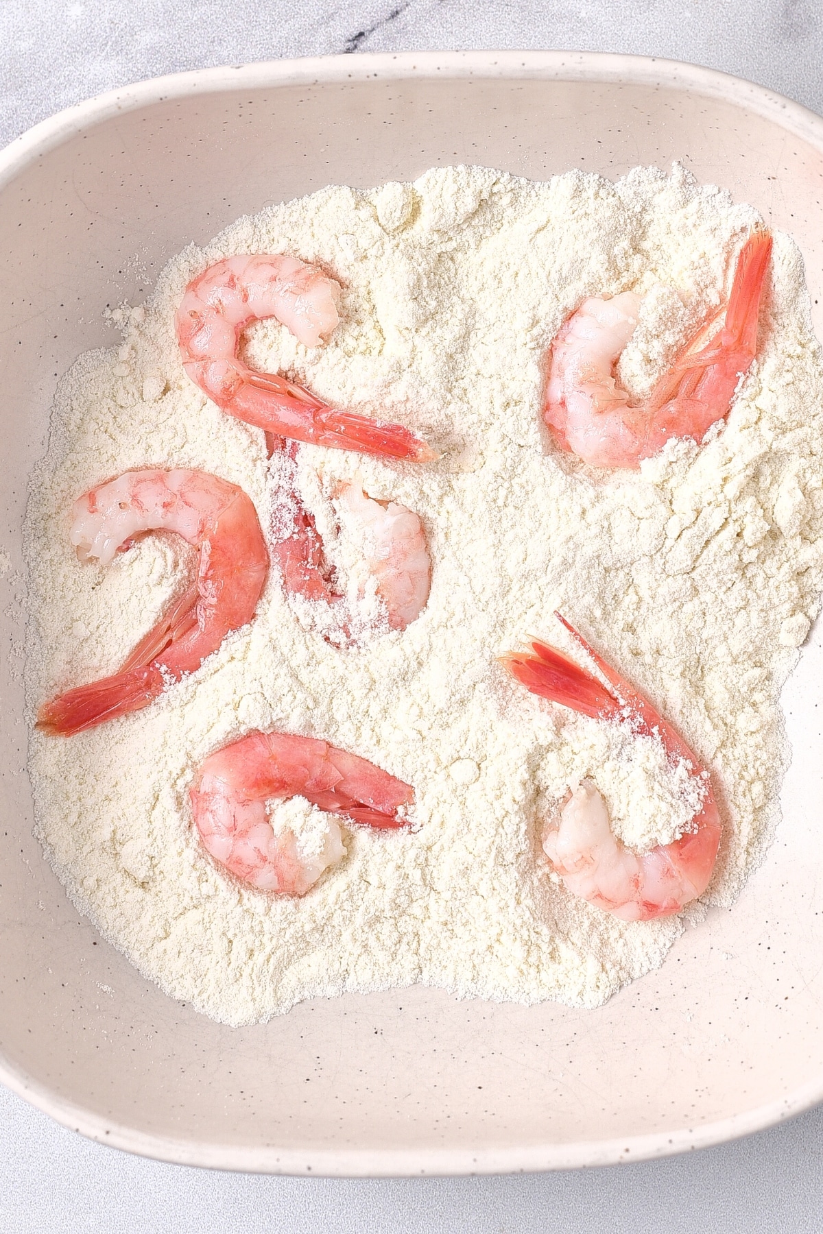 Coating fresh shrimp in flour in a bowl.