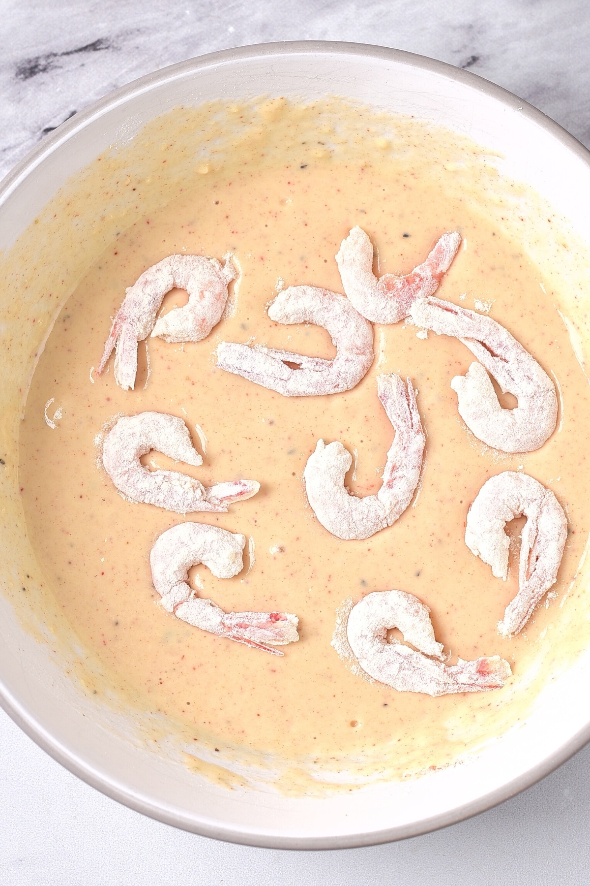 Floured shrimp on top of a bowl of batter.