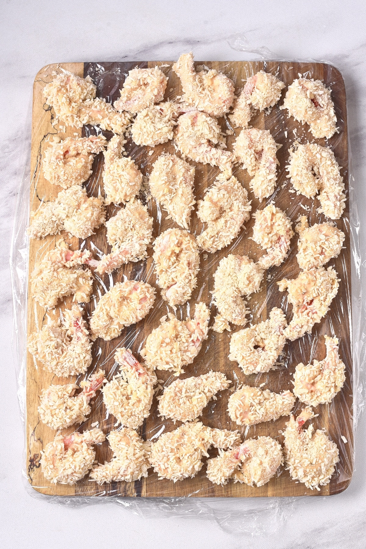 Freshly breaded shrimp on plastic-lined wooden board.