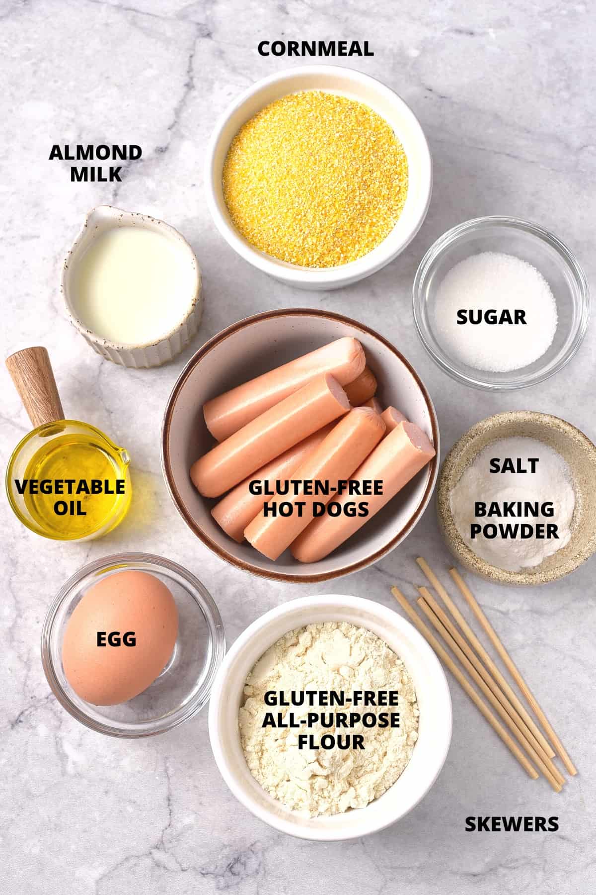 Ingredients for making gluten-free corn dogs laid out on marble board.