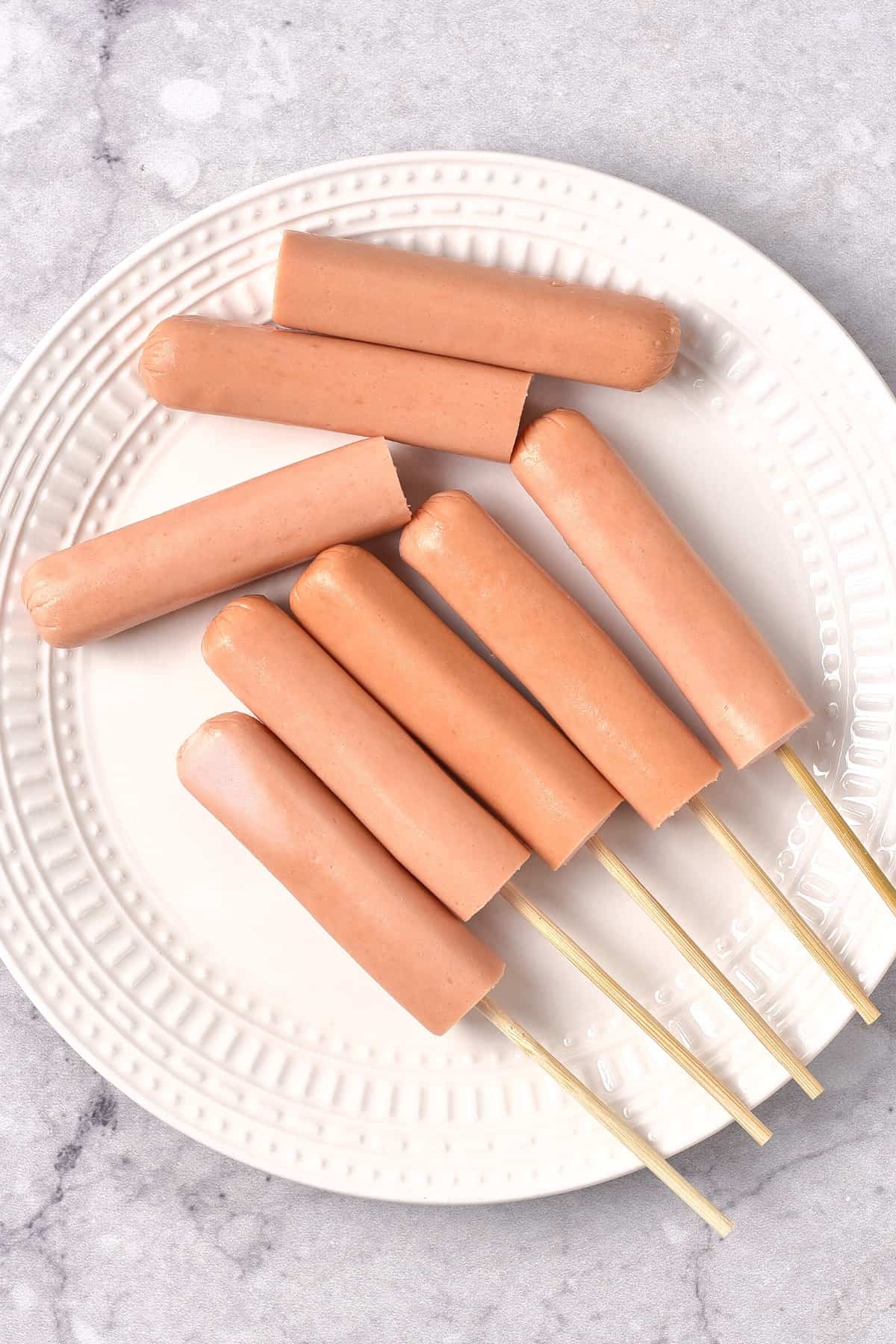 Hot dogs on skewers on white plate.