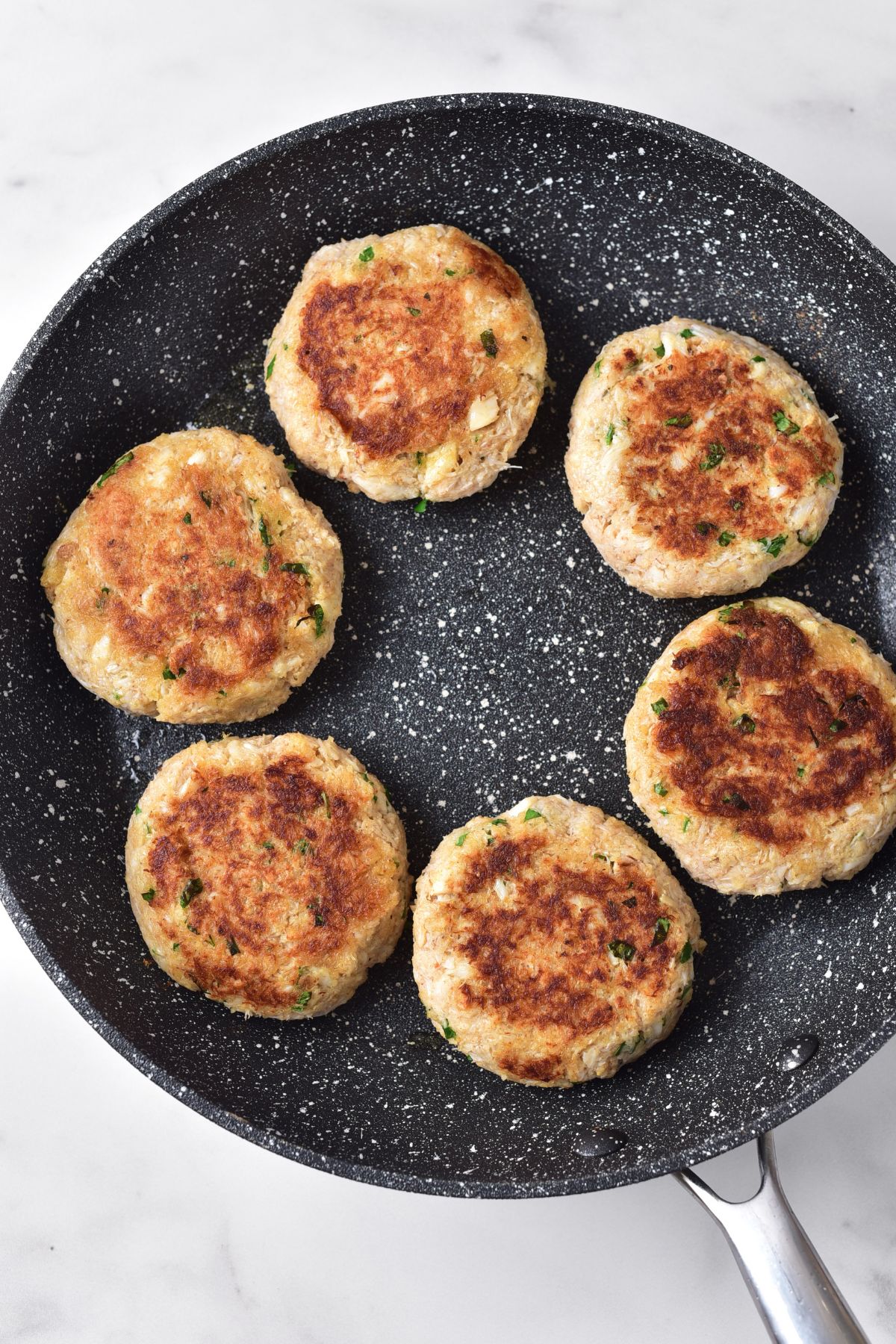 Pan frying crab cakes in skillet.