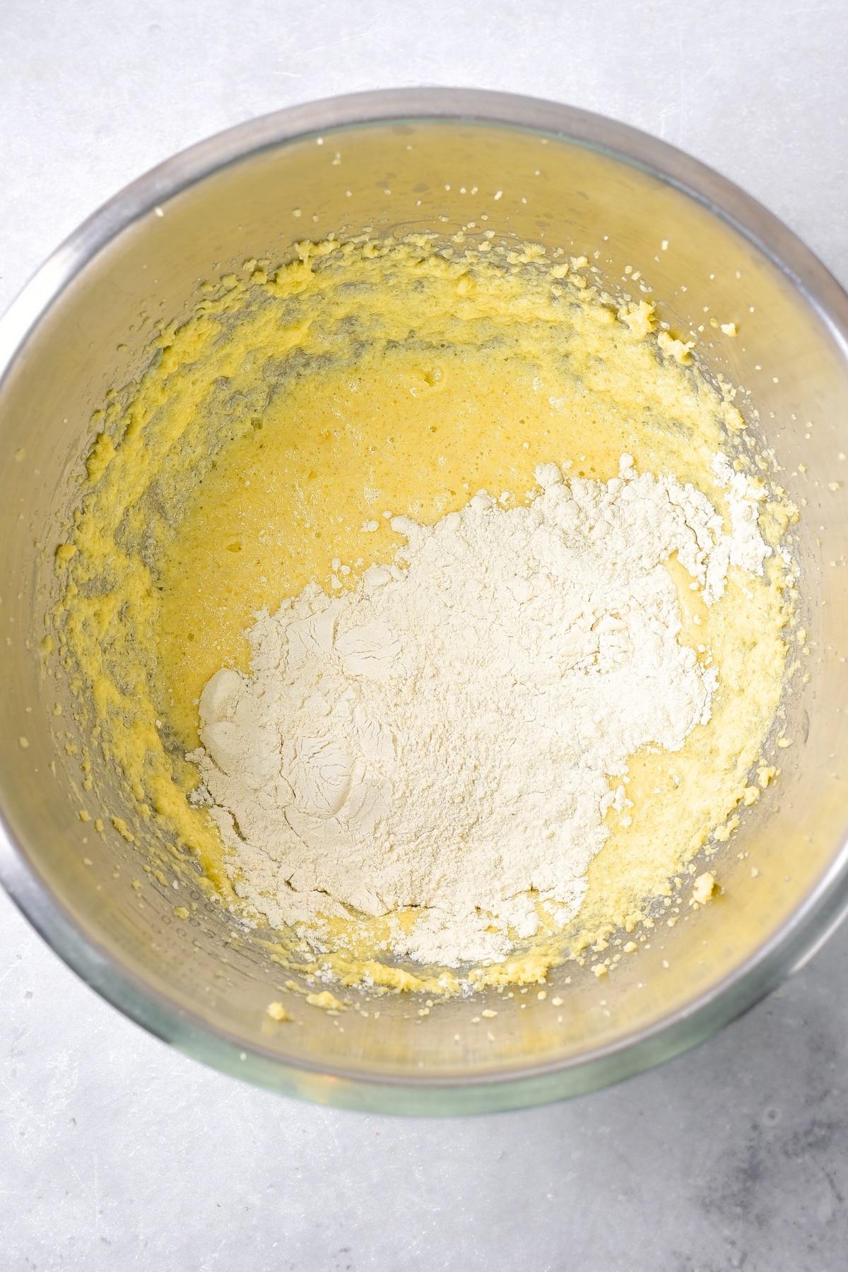 Flour mixture on top of pale yellow mixture in bowl.