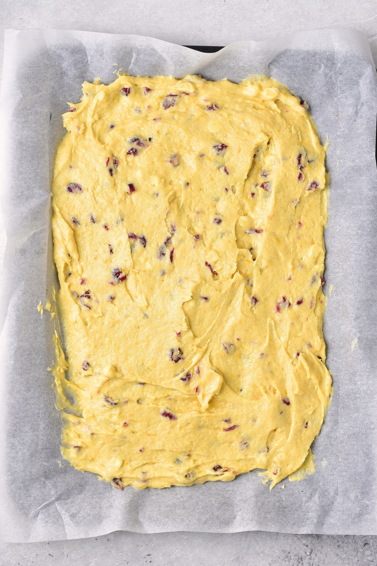 Cranberry cake batter spread out on parchment-lined baking pan.
