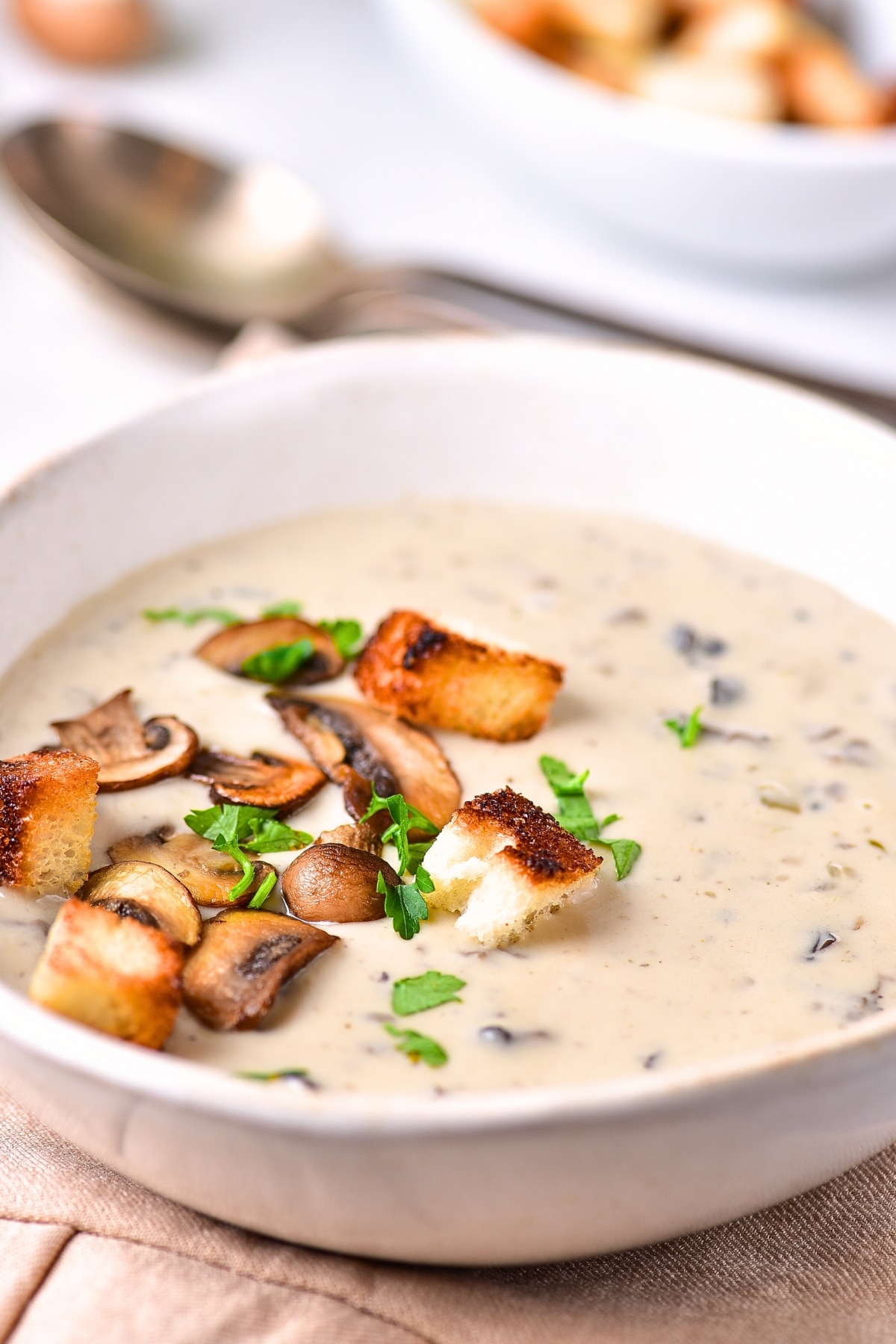 Up close view of bowl of mushroom soup topped with mushrooms and croutons.