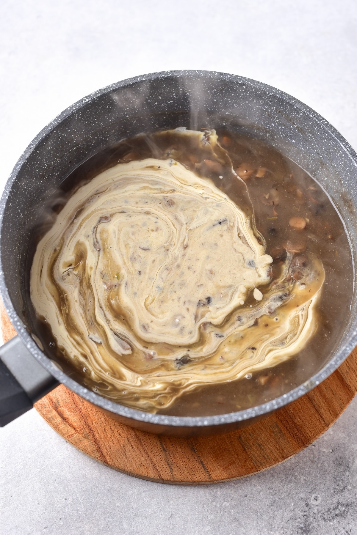 Cream mixed into a pot of mushroom soup.