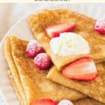 Up close shot of a plate of gluten-free crepes topped with cream and berries.