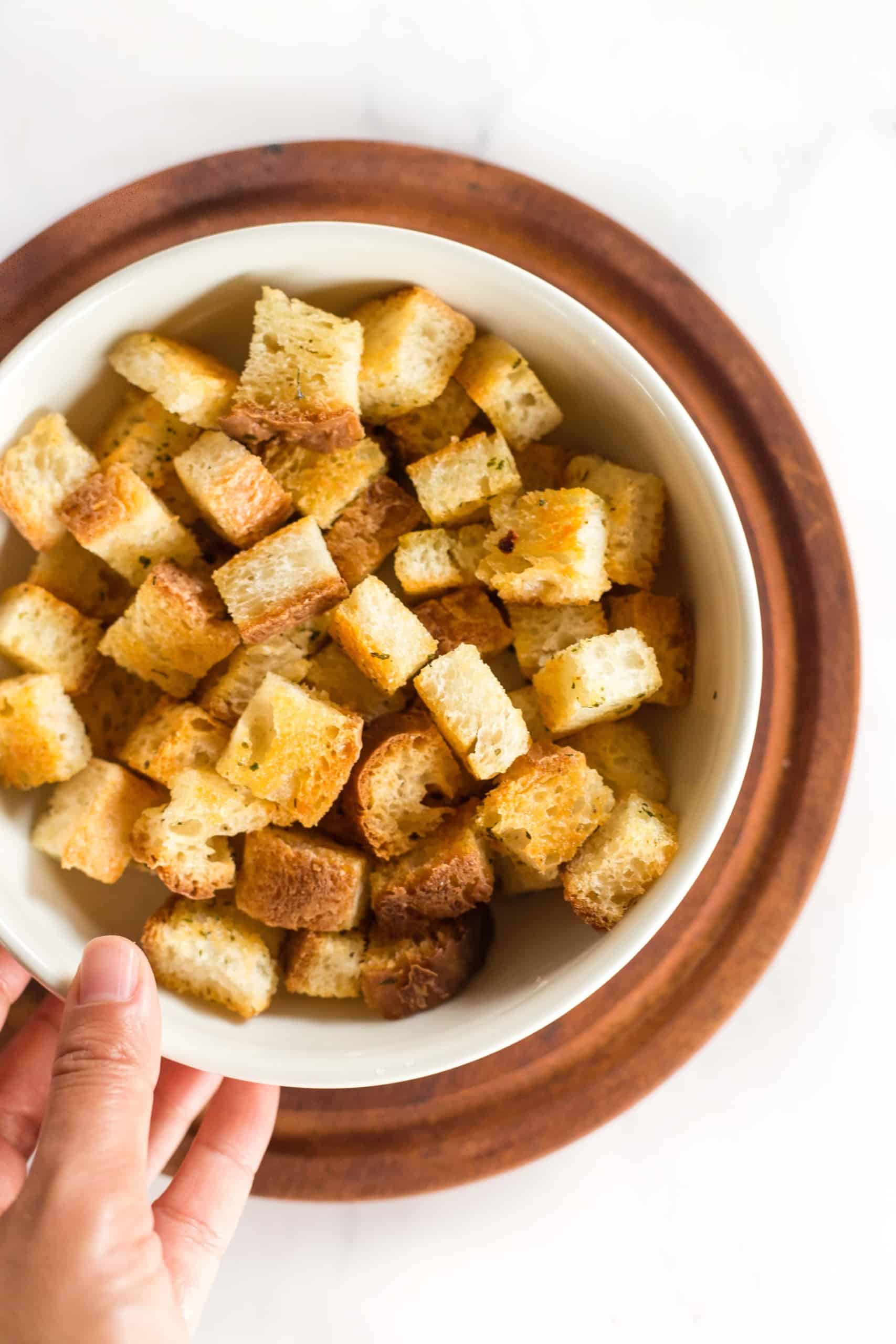 Hand reaching for a bowl of homemade gluten-free croutons.