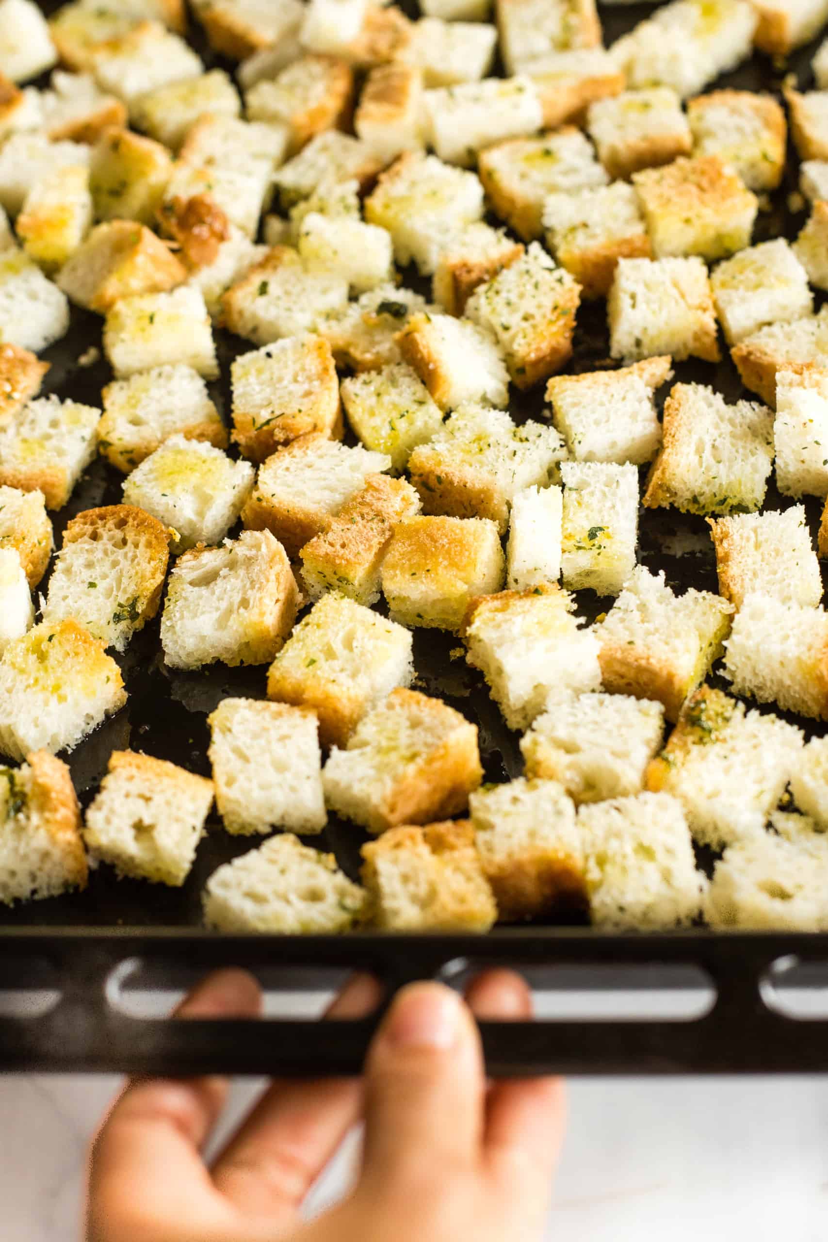 Bread cubes coated with oil and herbs spread out on baking sheet.