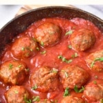 Gluten-free meatballs simmering in a pan of marinara sauce.