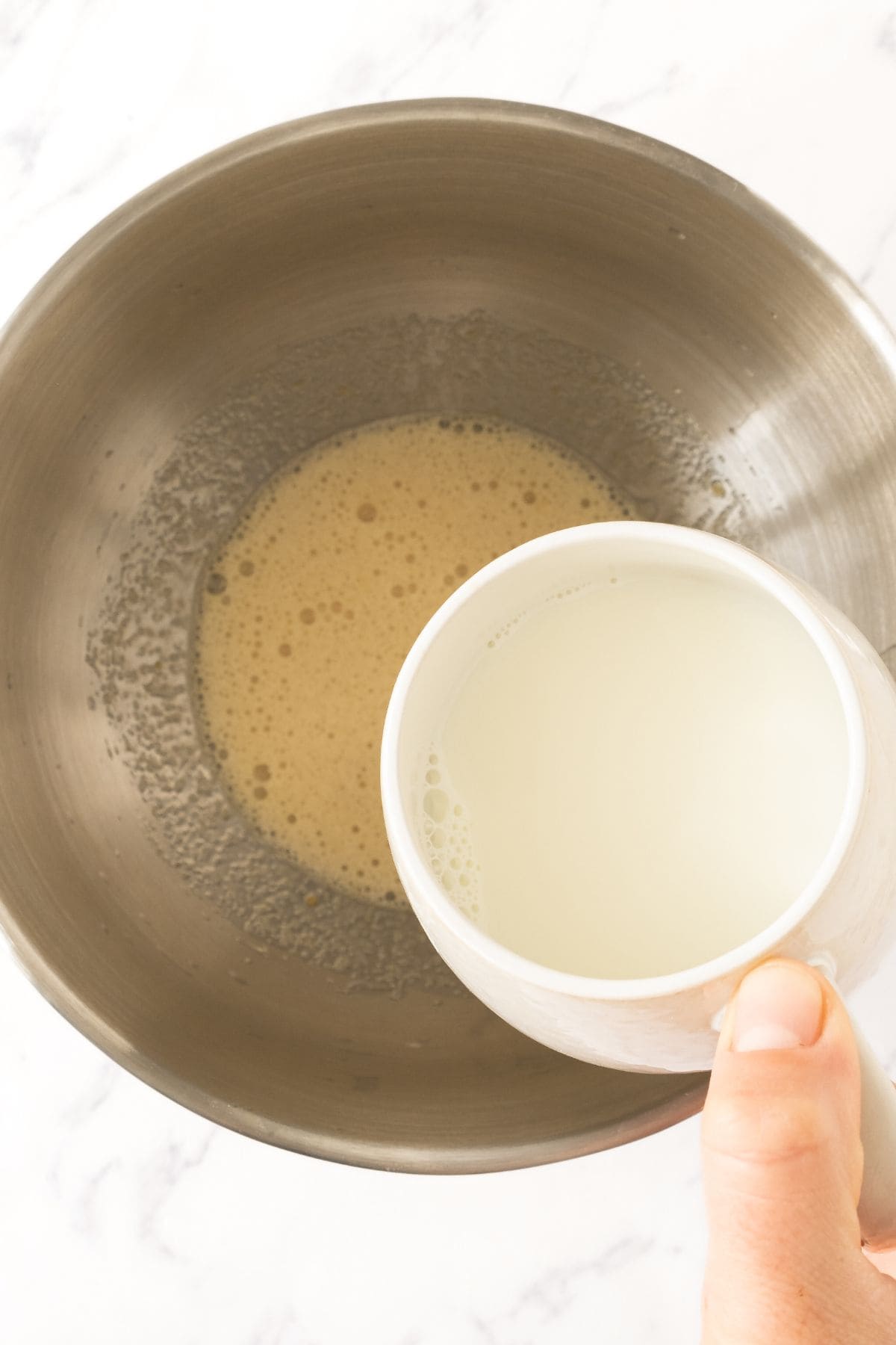 Pouring milk into a bowl of pale yellow mixture