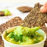 Dipping flaxseed meal cracker into a bowl of guacamole.