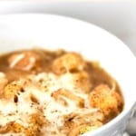 A bowl of soup topped with croutons and cheese.