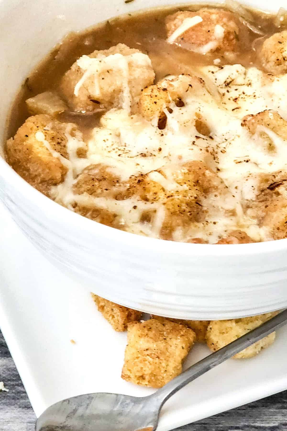 A bowl of gluten-free onion soup on a white plate.