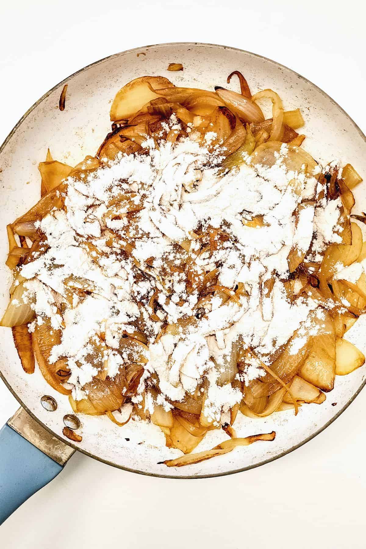 Flour sprinkled on top of caramelized onions in skillet.