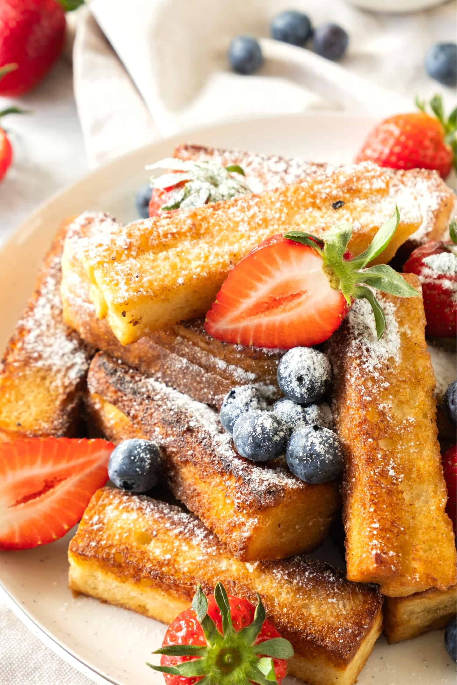 A plate of gluten free French toast sticks and berries sprinkled in powdered sugar.