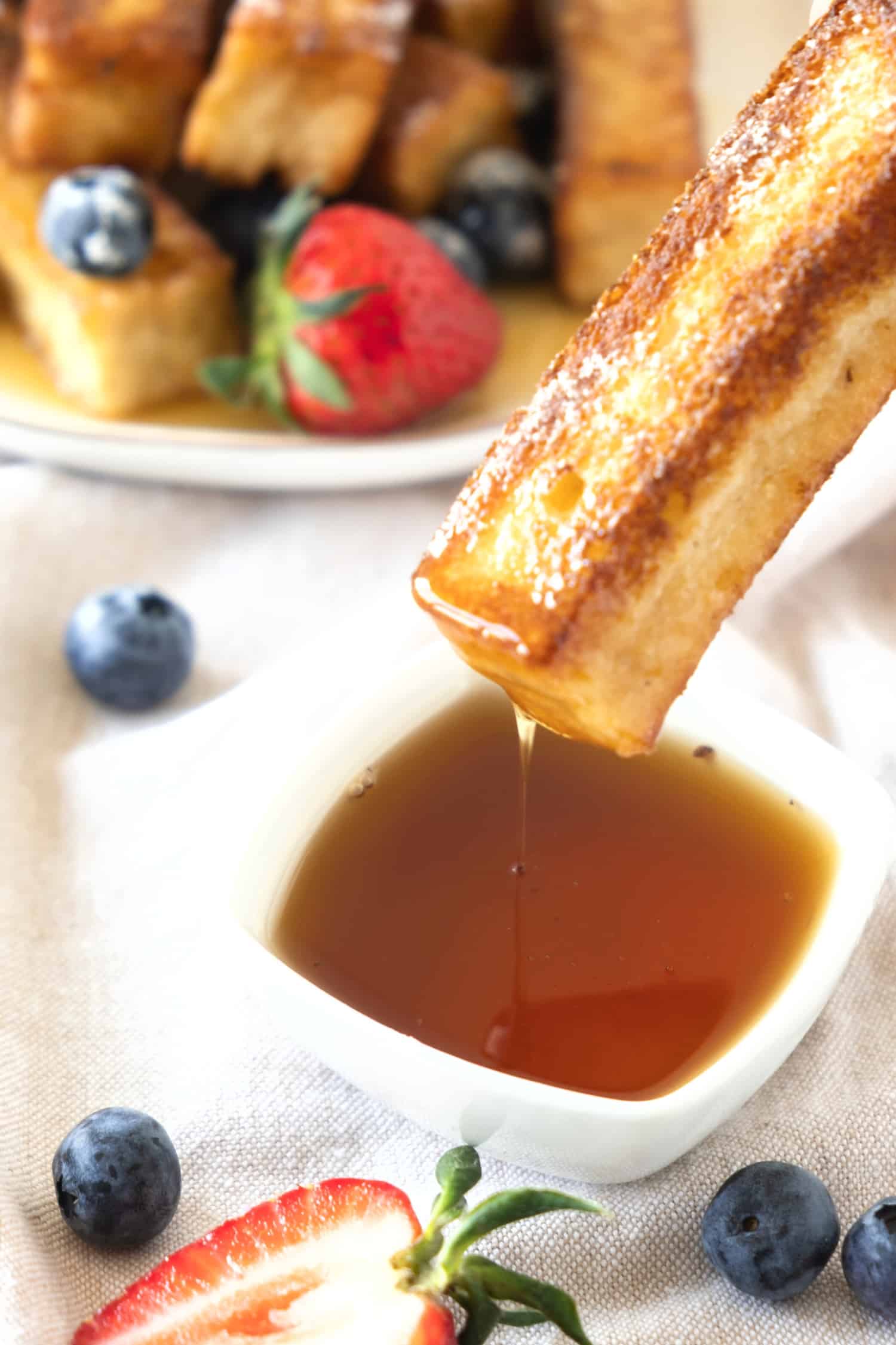 Dipping a French toast stick into a small bowl of maple syrup.