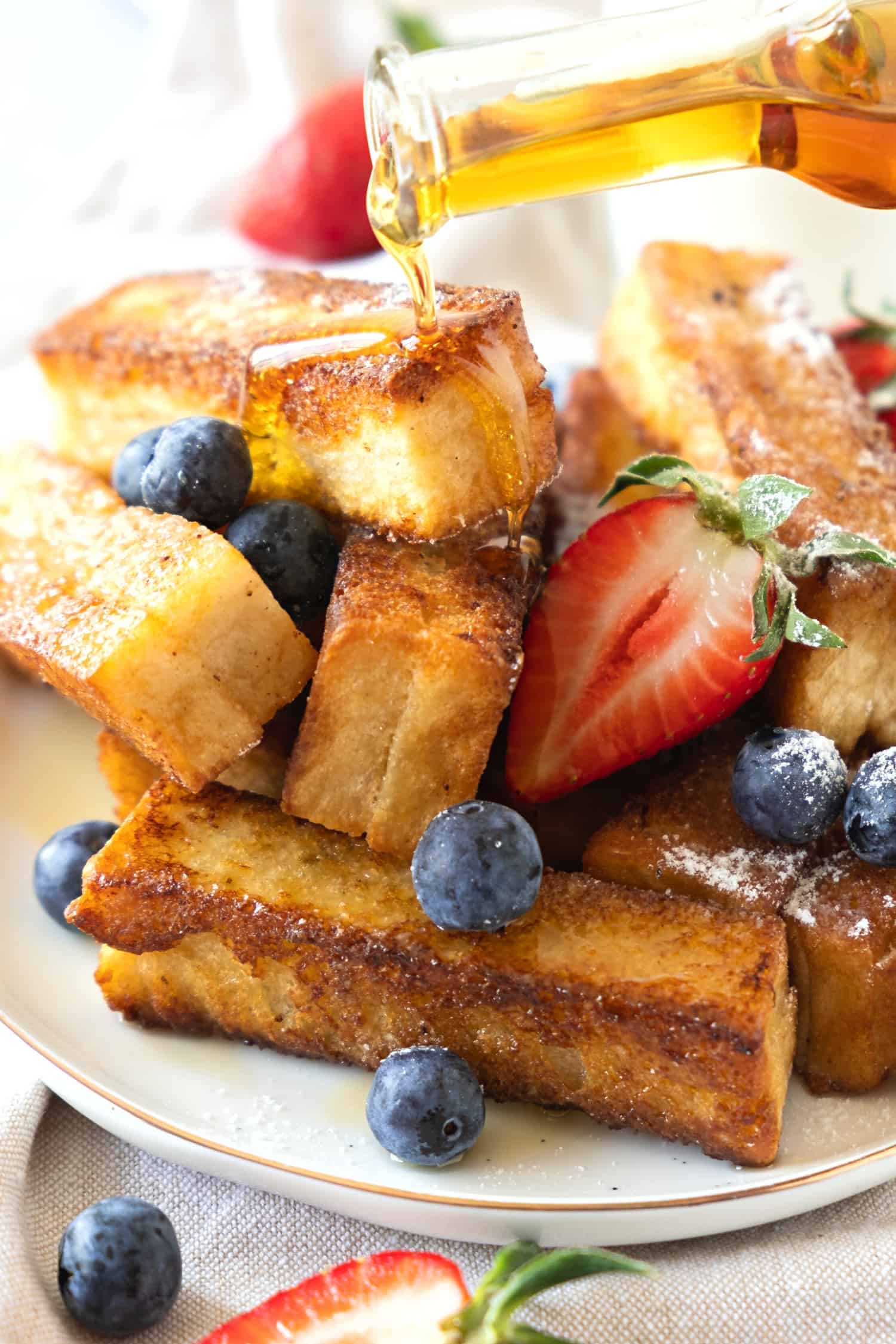 Pouring maple syrup over a plate of fresh berries and French toast sticks.