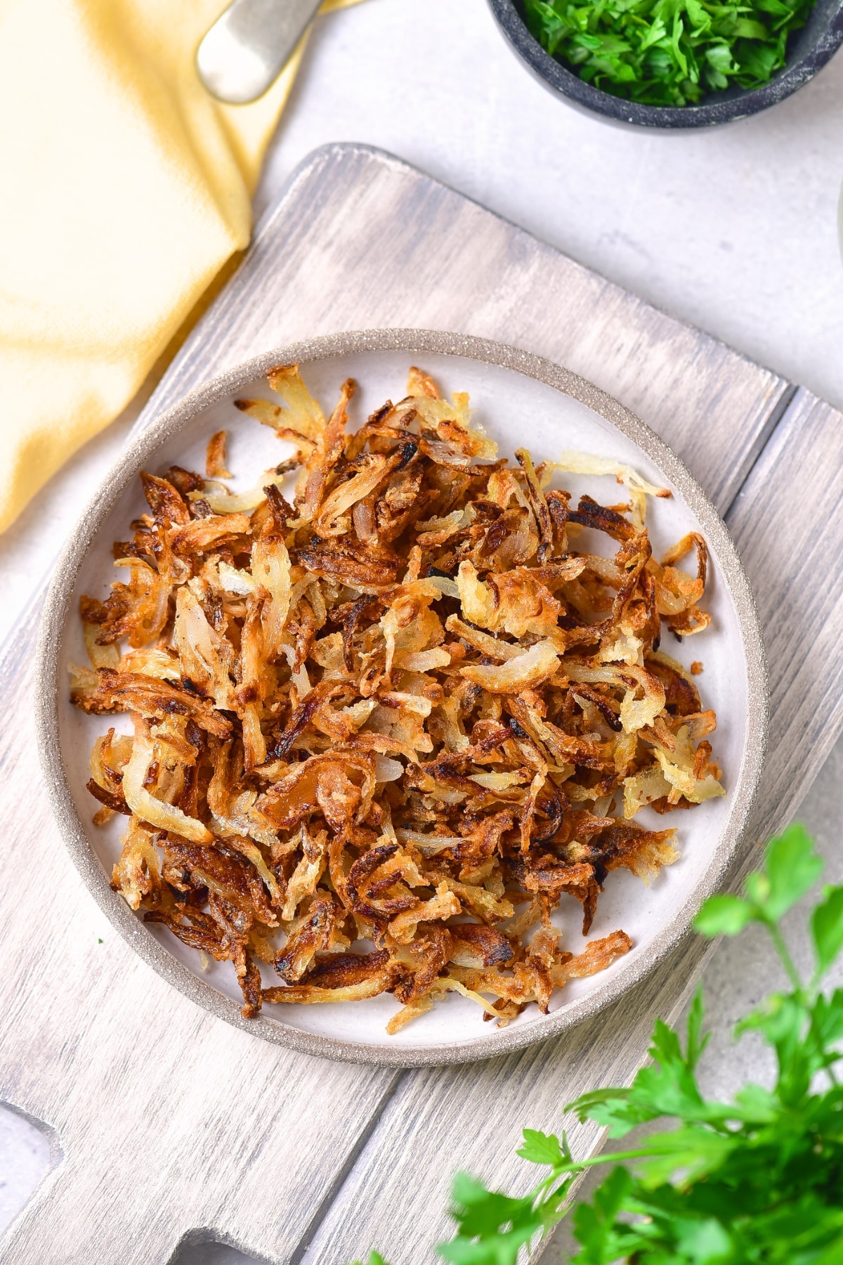 Top down view of a plate of gluten-free crispy fried onions on wooden board.