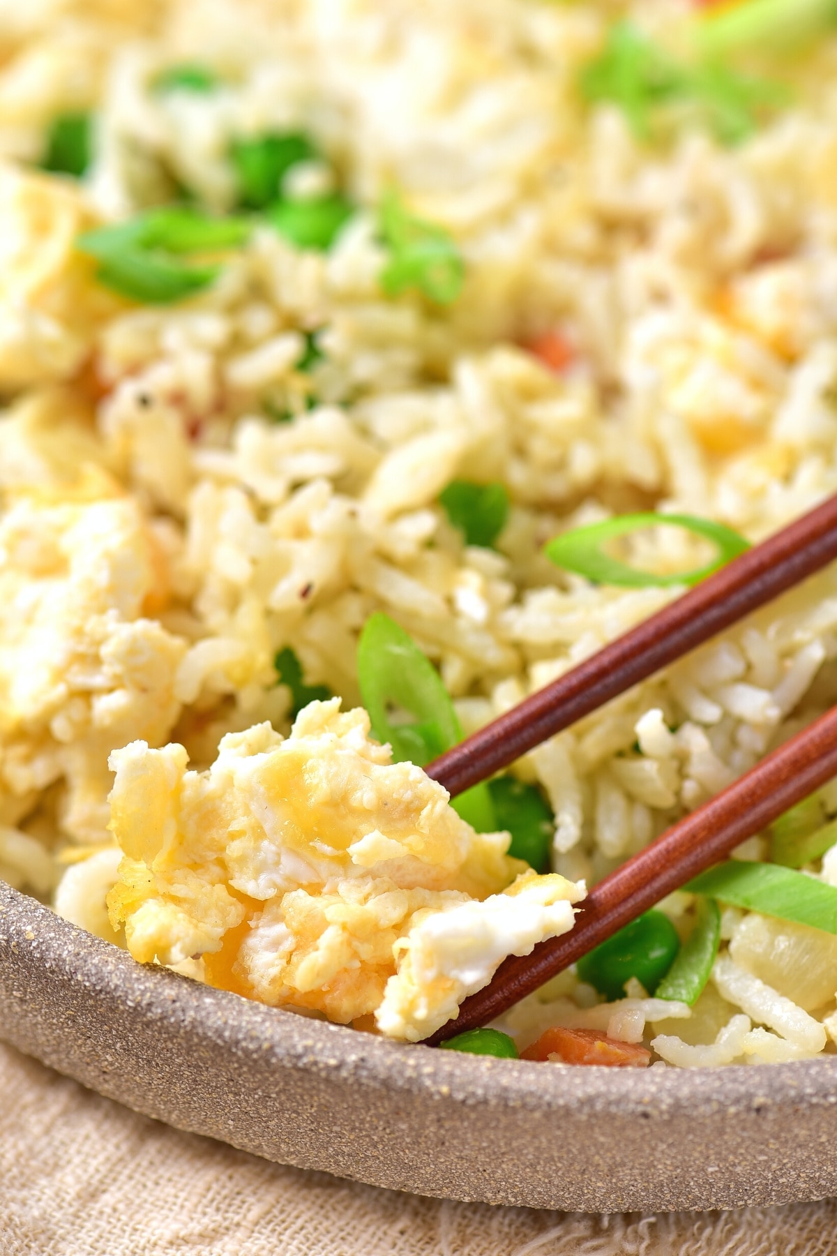 Chopsticks picking up a piece of egg from a bowl of gluten-free fried rice.