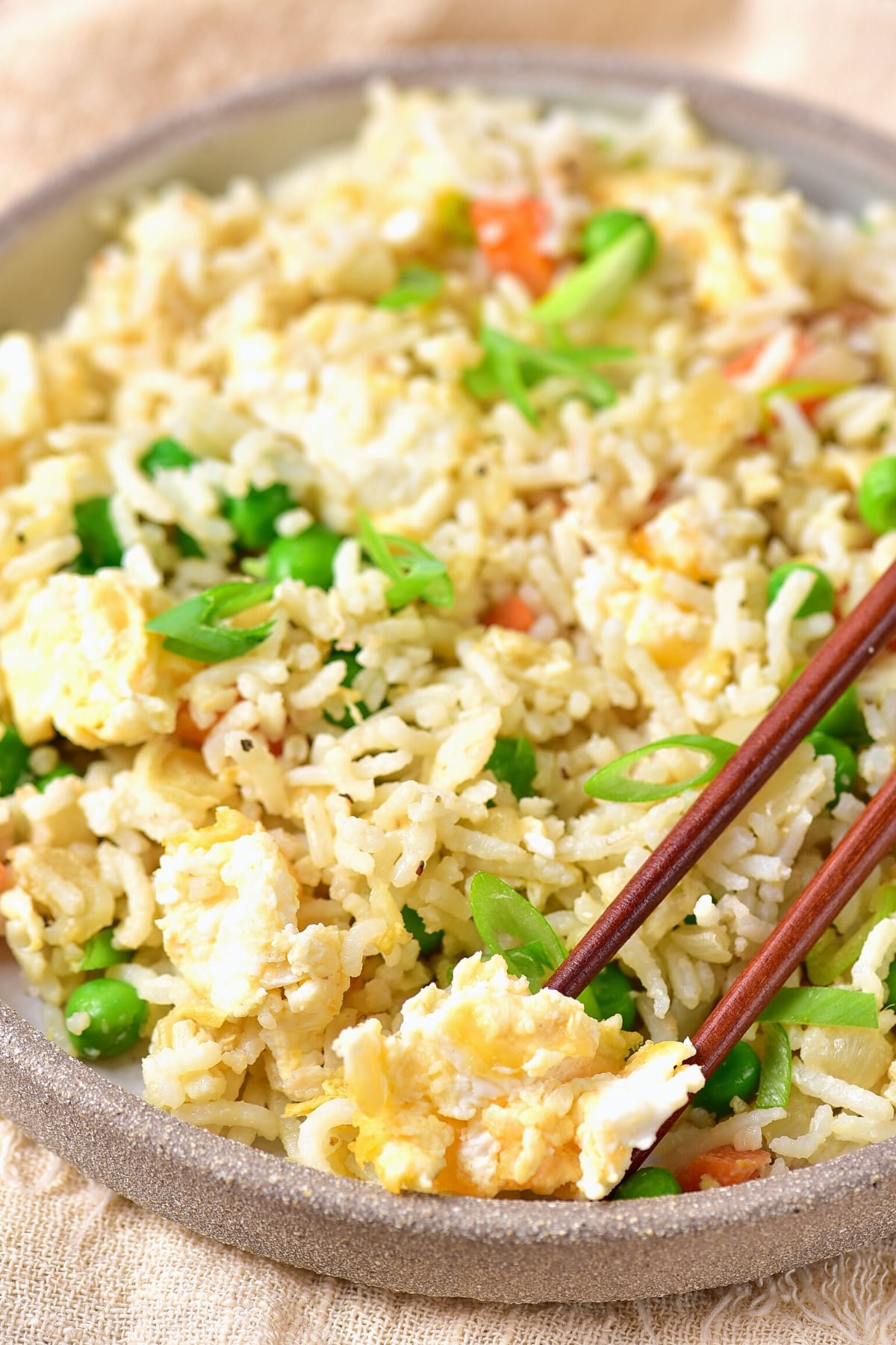 A pair of chopsticks picking up egg from a bowl of gluten-free egg fried rice.