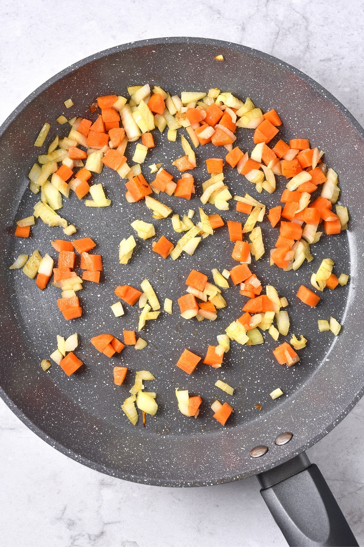Sautéing diced carrots and onions in a skillet.