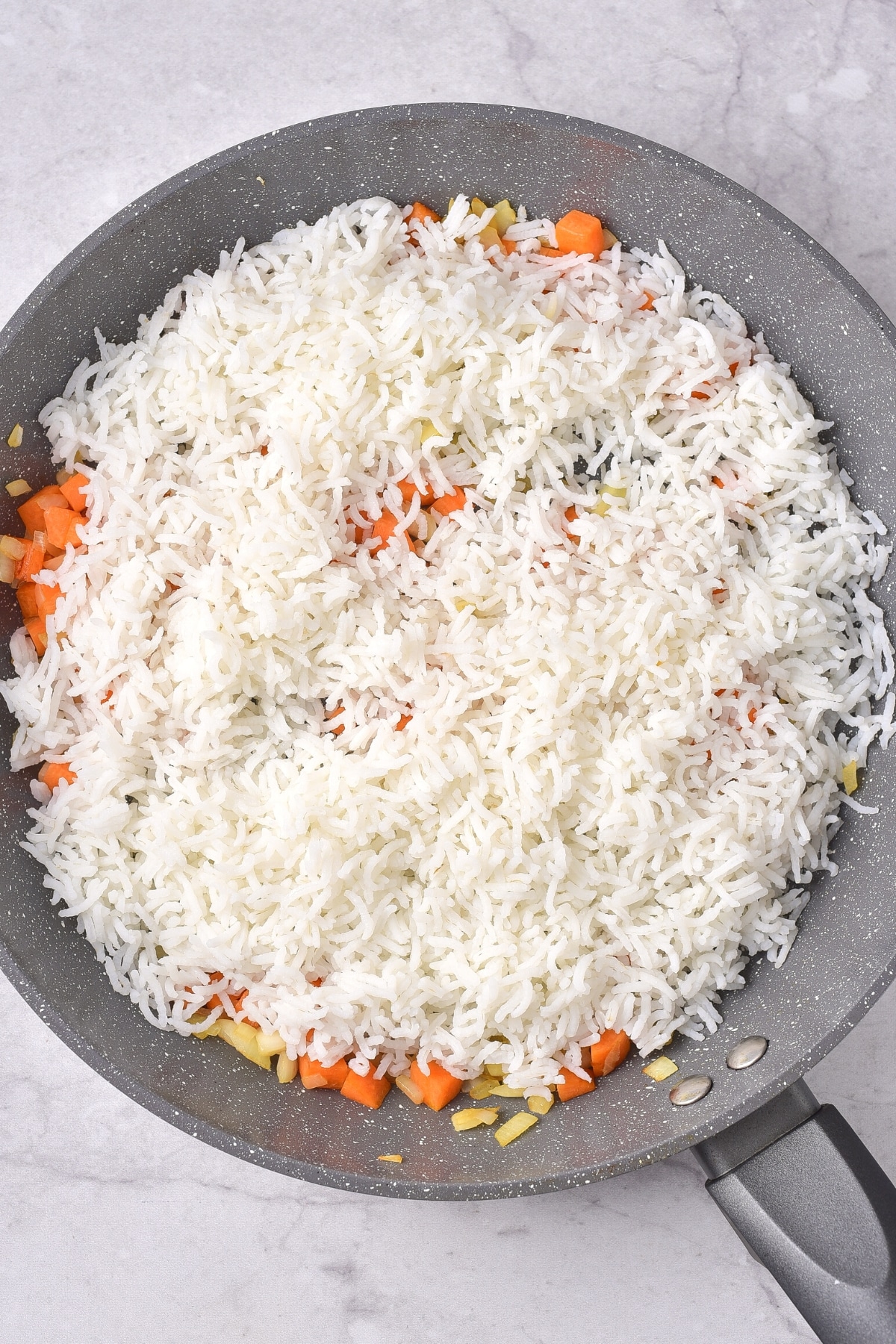 A large skillet with sautéed carrots, onions and cooked white rice.