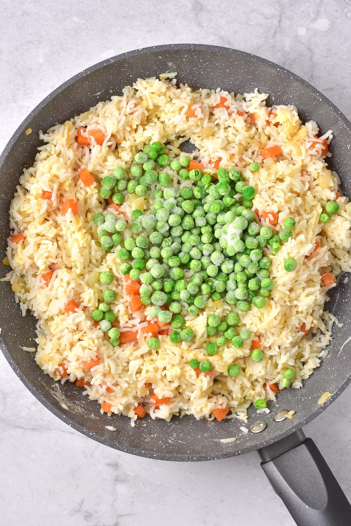 Frozen peas on top of a skillet of gluten-free fried rice.