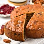 A half-sliced fruit cake on wooden board