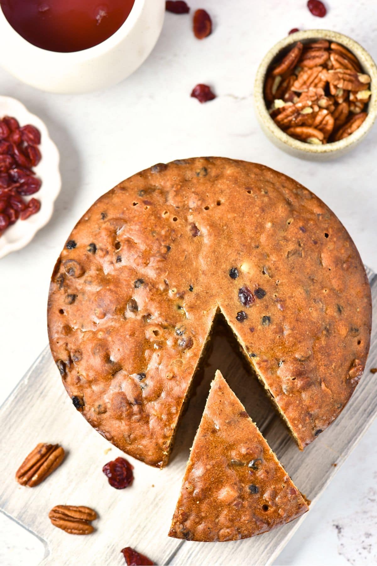 Top down view of half-sliced fruit and nut cake on wooden board.