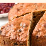Half-sliced gluten-free fruitcake on wooden board.