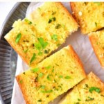 Sliced garlic baguette on parchment-lined plate.