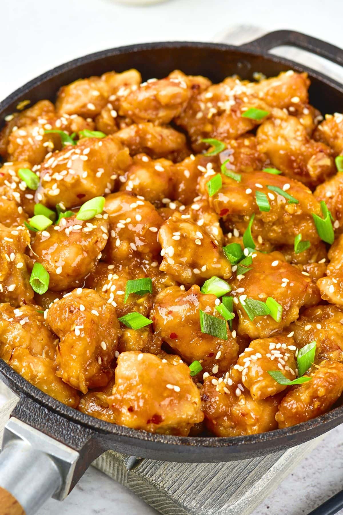 A skillet with general tso chicken sprinkled with chopped green onions