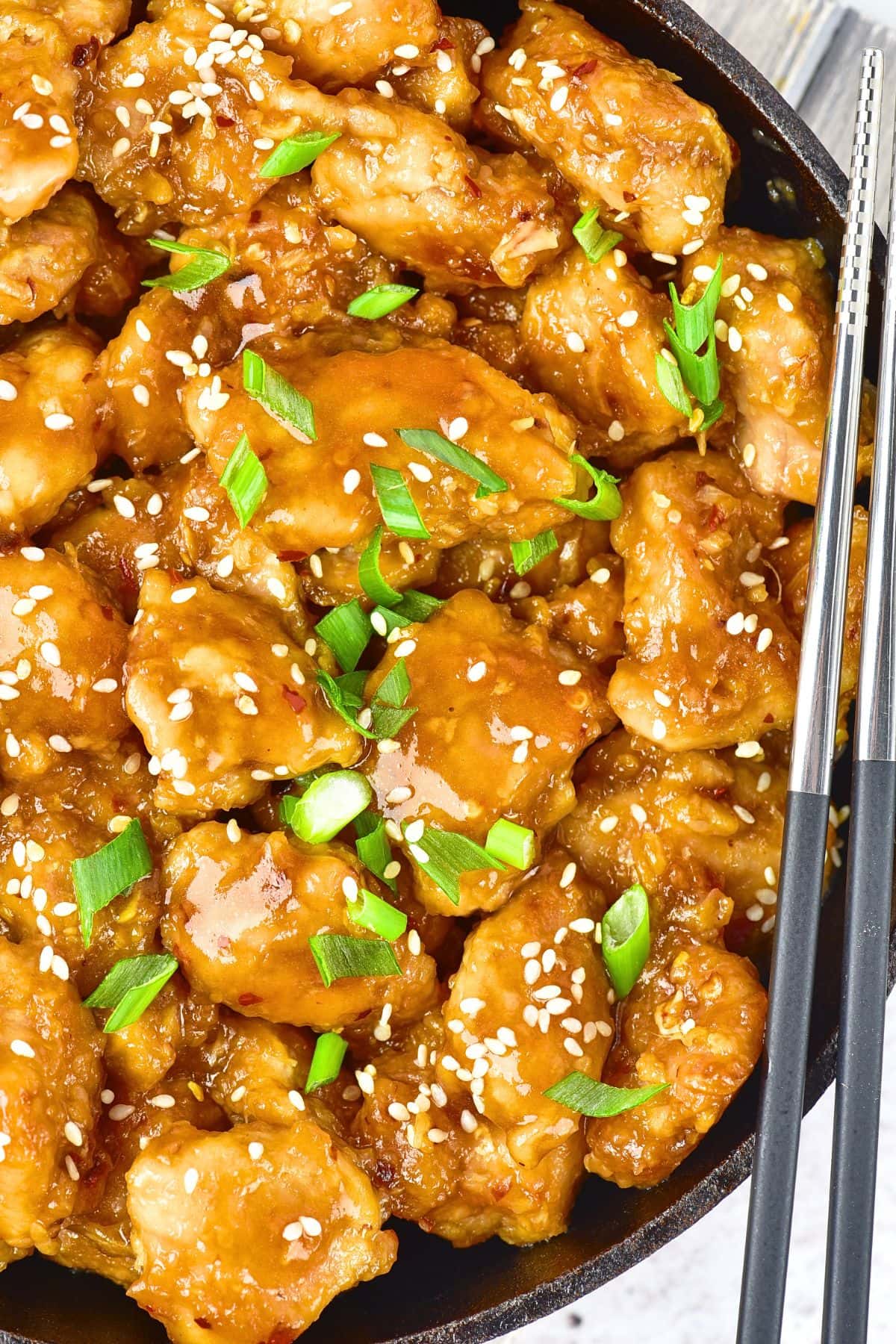 Top down view of green onions on top of skillet of chicken in sauce