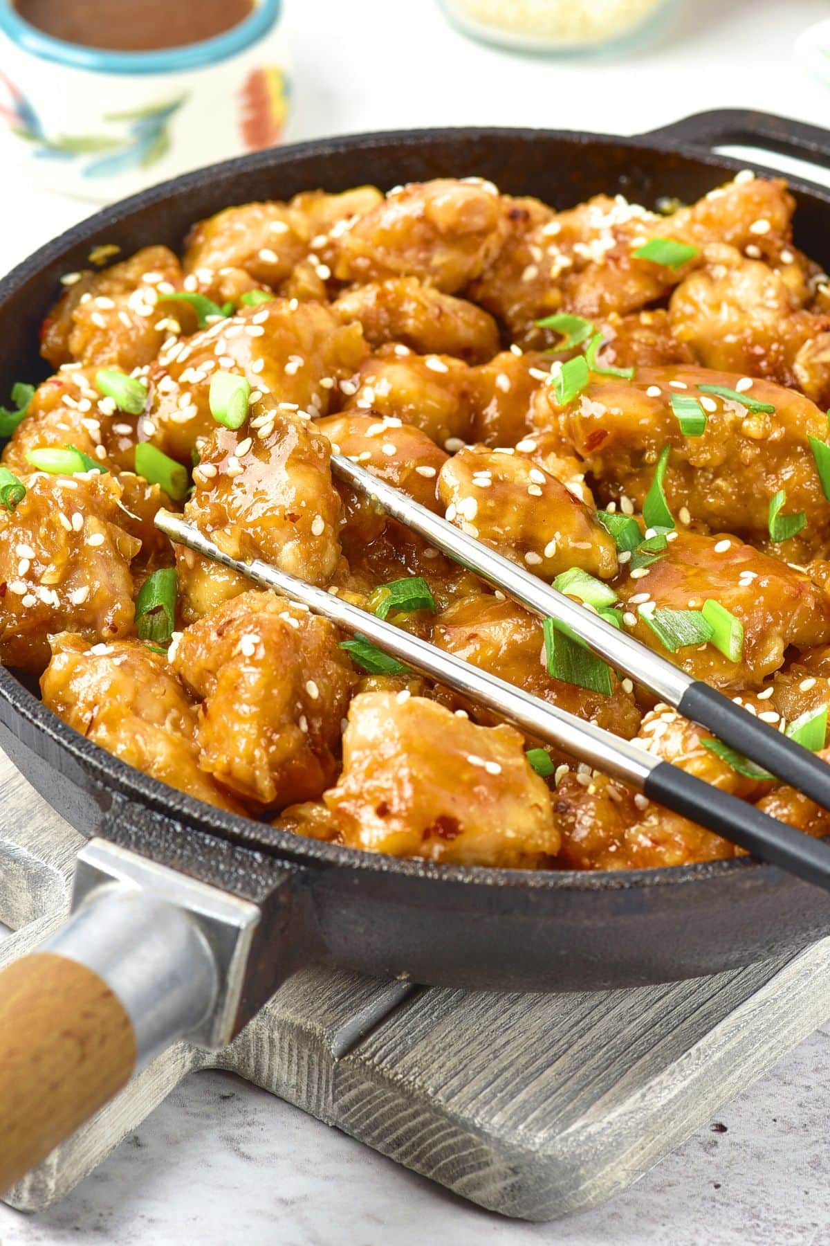 Chopsticks on top of a skillet with chicken in sauce