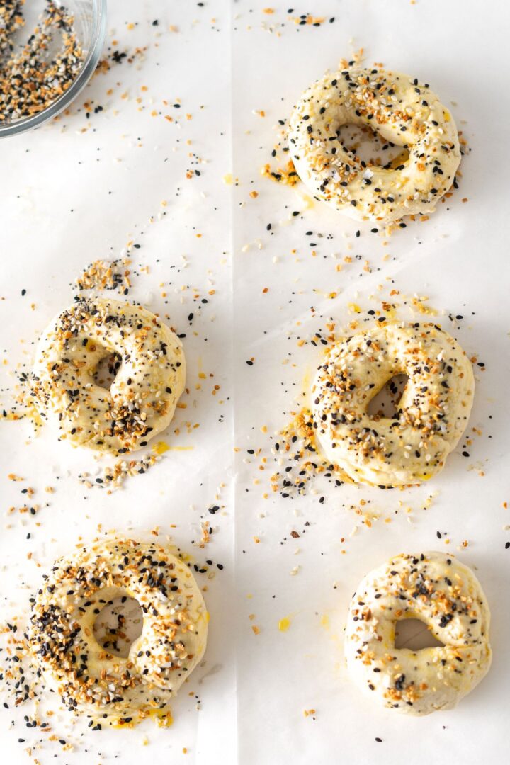 Shaped bagel dough topped with everything bagel seasoning on parchment paper.