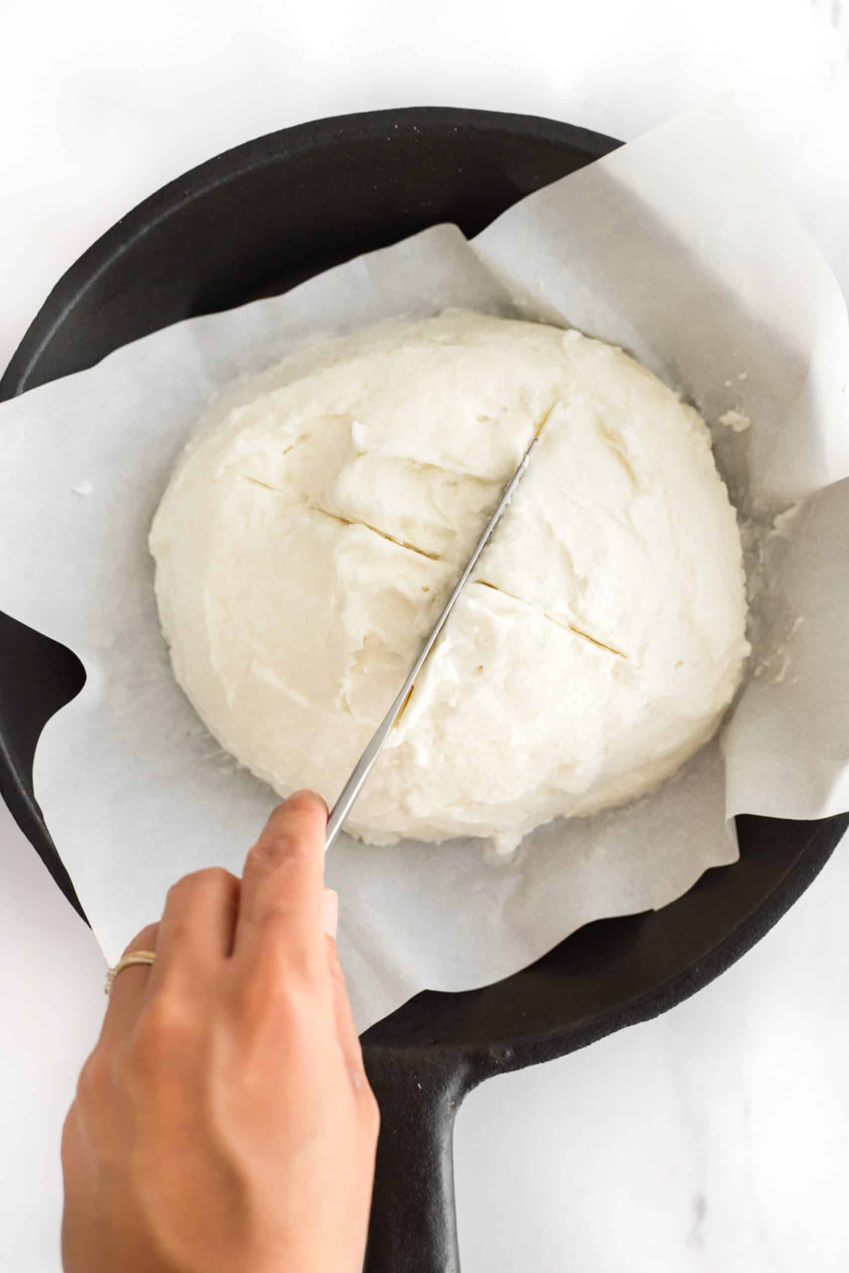 Using a knife to cut a cross on top of the bread dough.