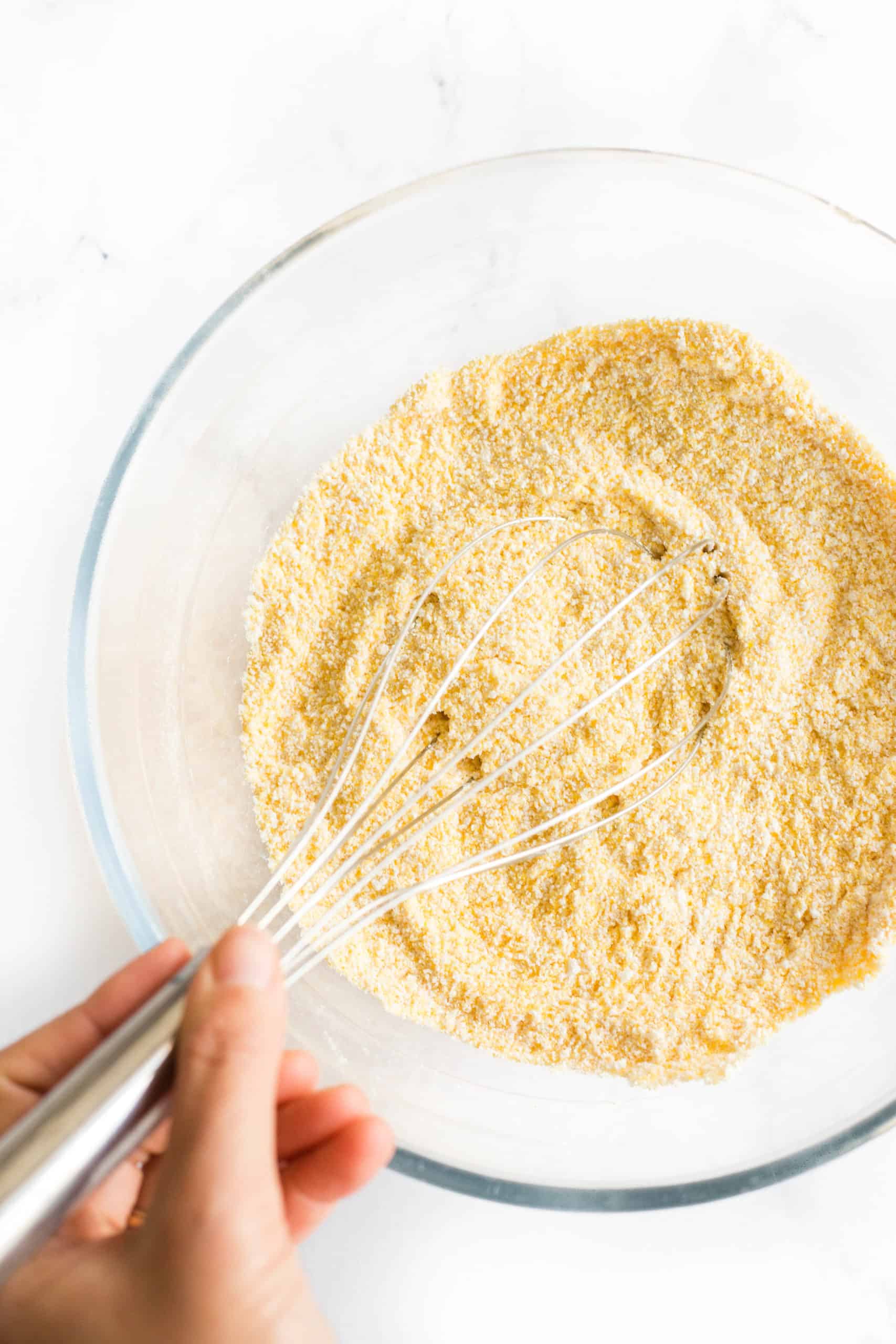Hand whisking dry ingredients in a glass mixing bowl. 