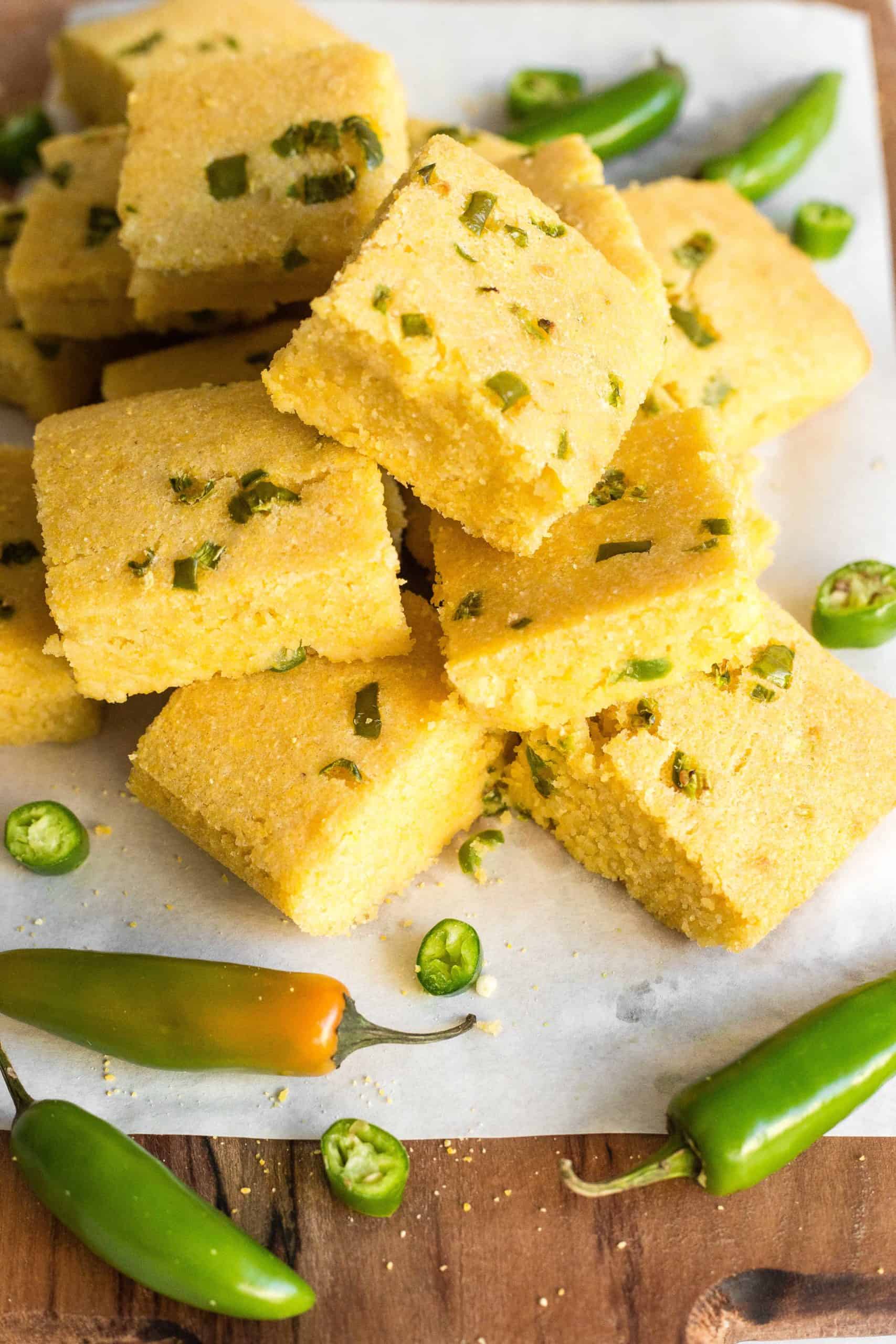 A stack of gluten-free jalapeno cornbread squares on a parchment-lined wooden board.