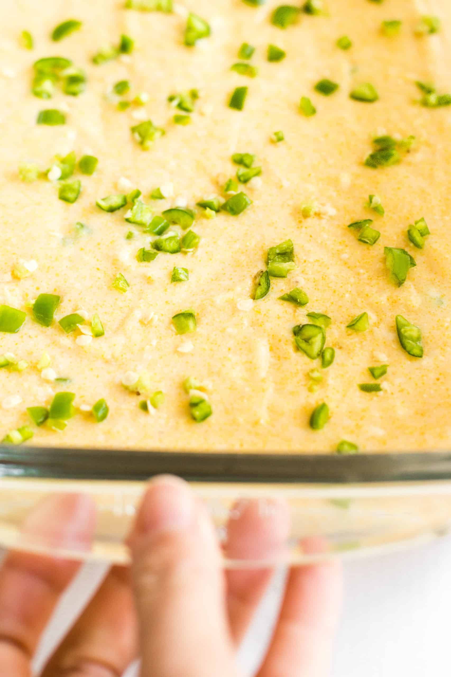 Hand holding a glass baking dish with gluten-free jalapeño cornbread batter ready to be baked.