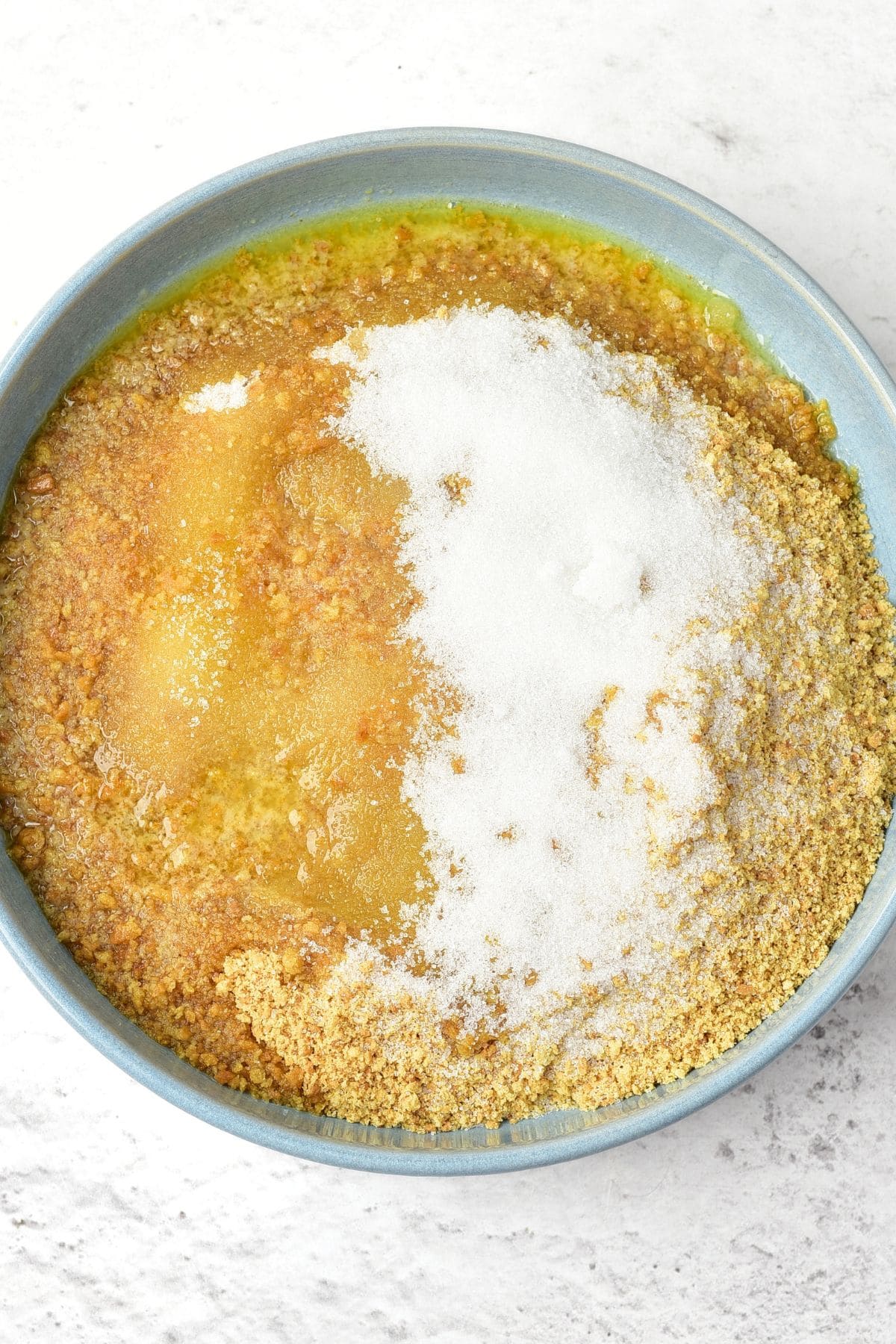 Graham cracker crumbs, sugar and butter in blue bowl